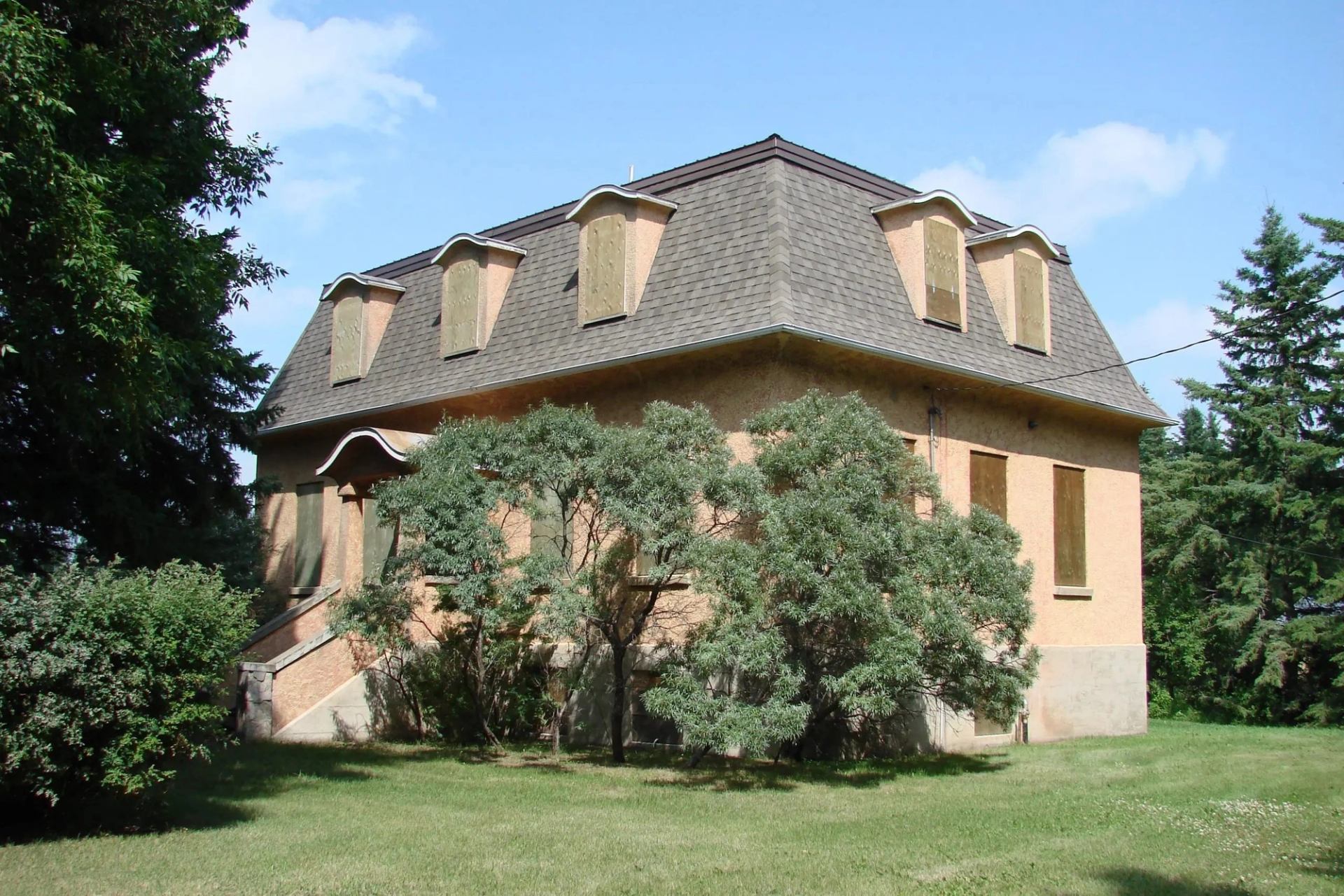 Two‑storey tan house with dormer windows and trees in front on the museum grounds.