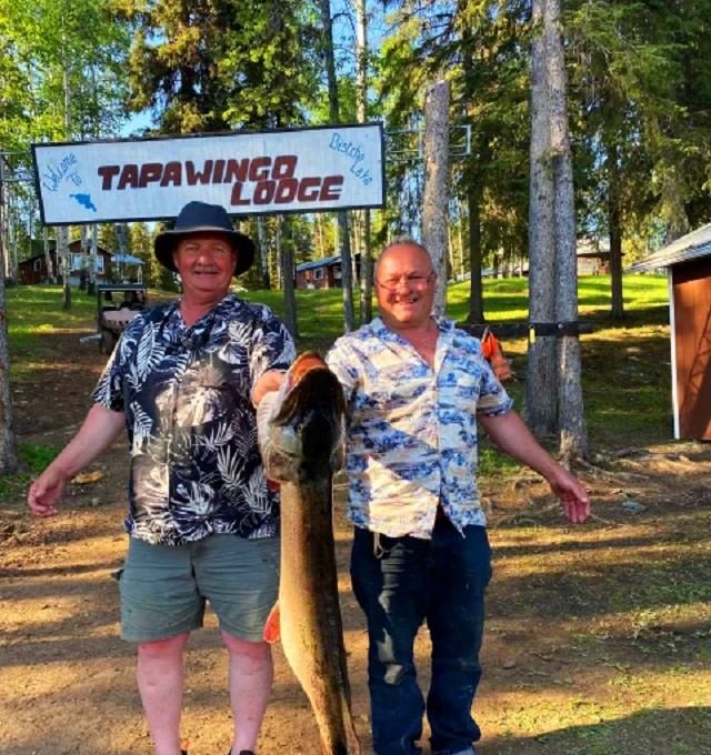 Two people holding a big fish in from of the lodge