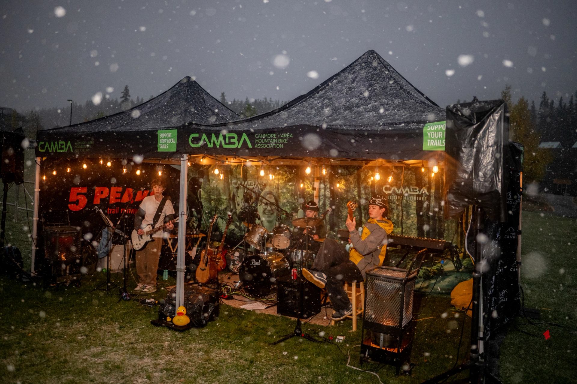Outdoor band performs under CAMBA tents with string lights during falling snow.