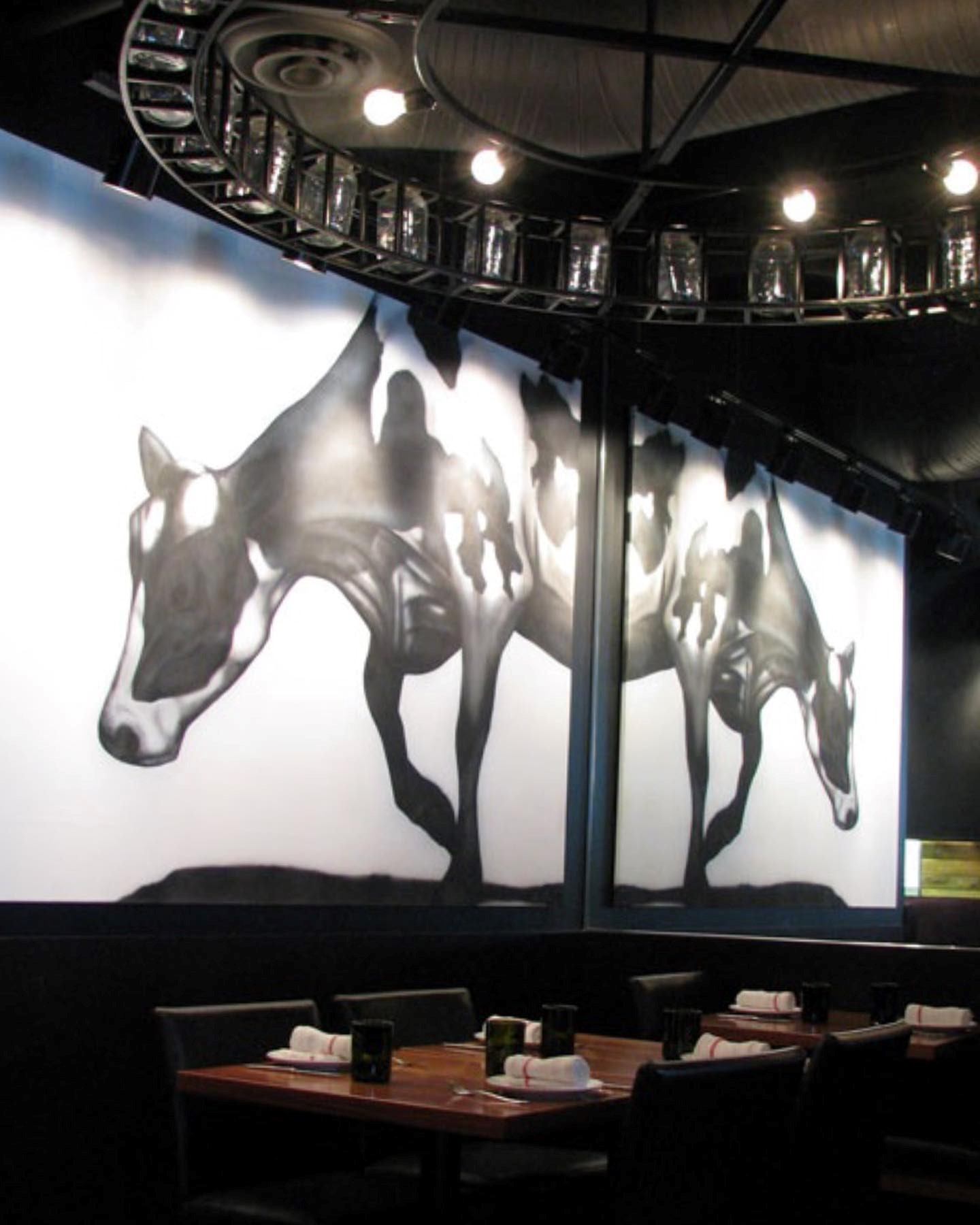 Abstract black and white mural featuring a distorted cow design across two panels. The overlapping figures create a dynamic, surreal effect under soft lighting.