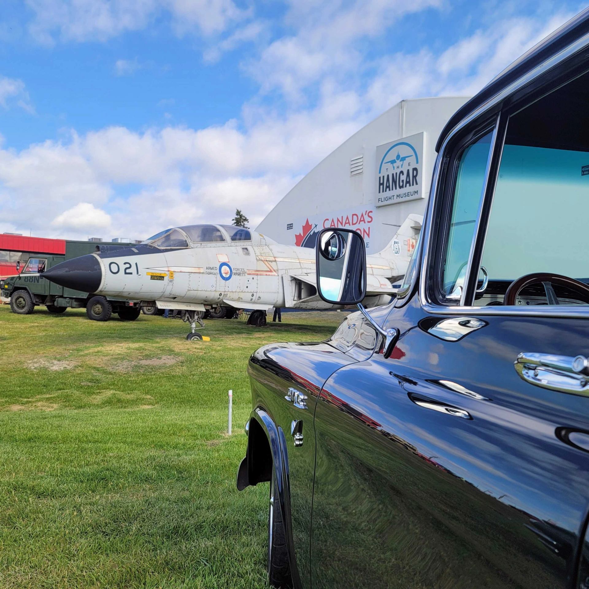 Vintage jet and black pickup truck parked outside The Hangar Flight Museum building.