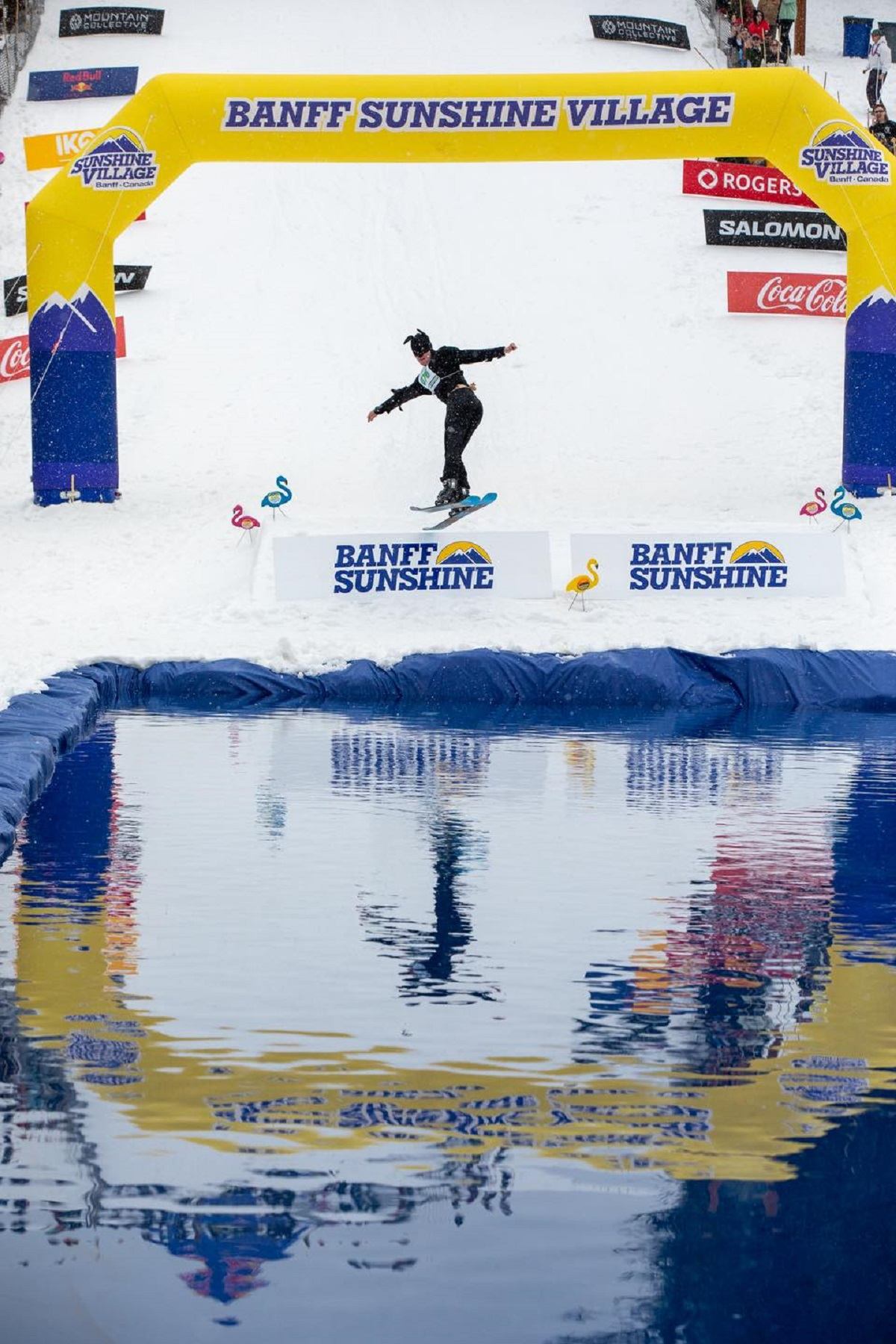 Snowboarder approaching a water pool at the Slush Cup event beneath a Banff Sunshine Village arch.