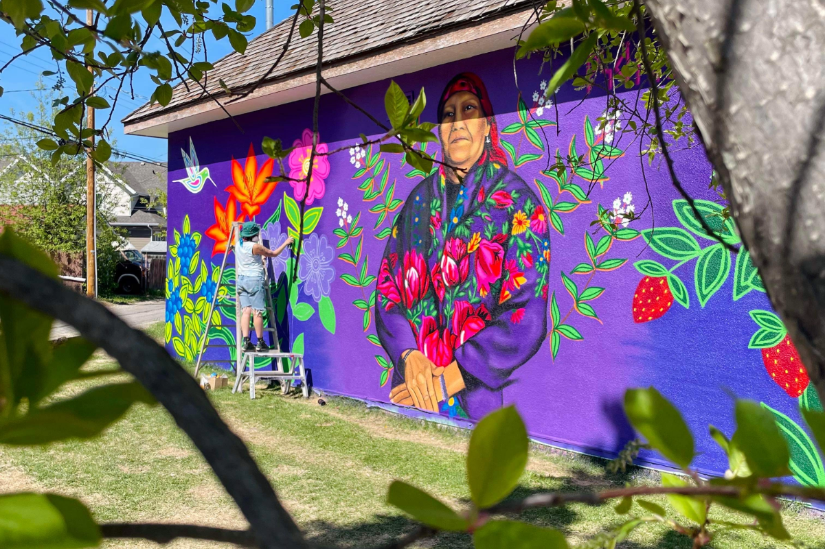 Artist painting a vibrant floral mural on a purple wall.