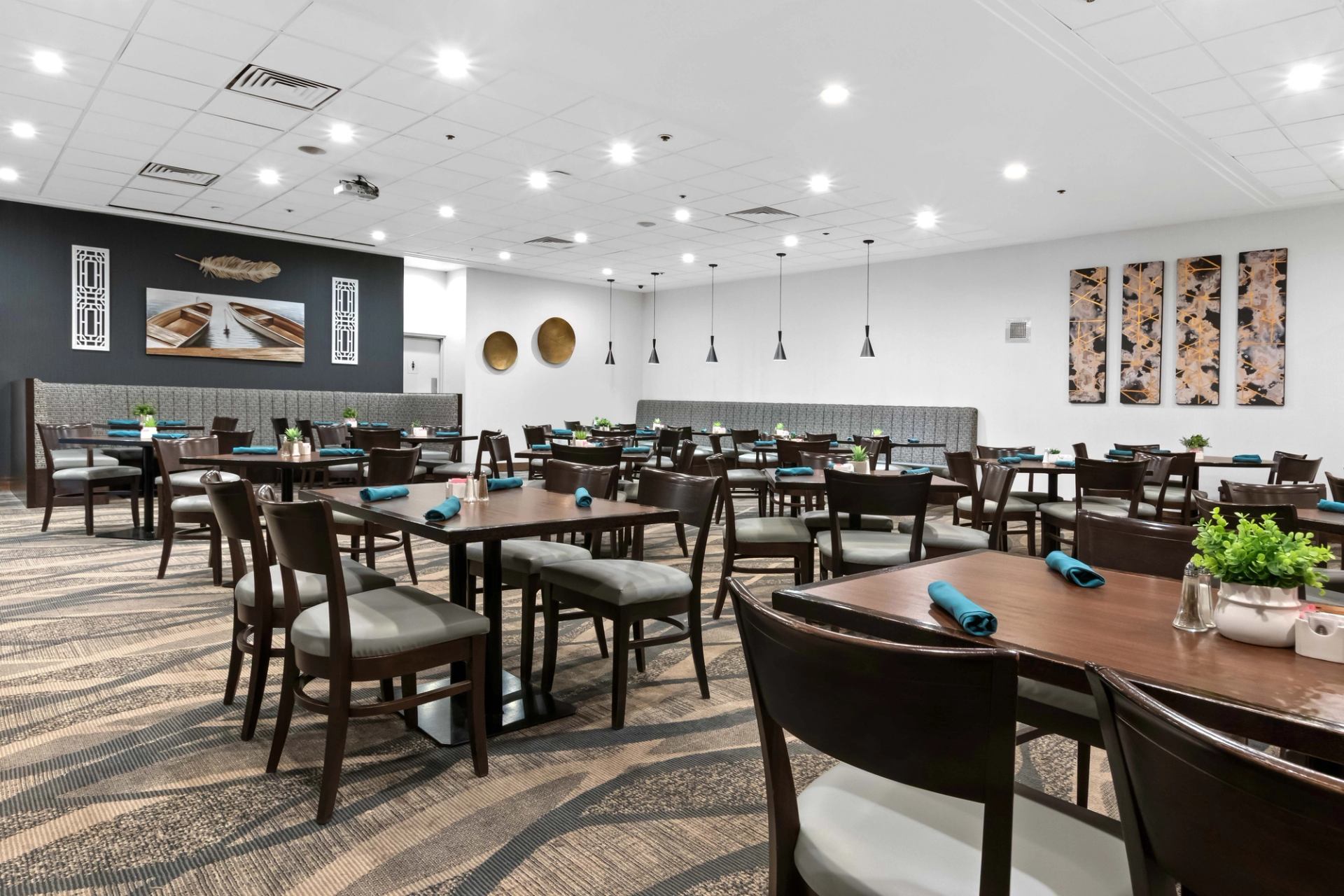 Modern dining room with wooden tables, teal napkins, pendant lights and wall art.