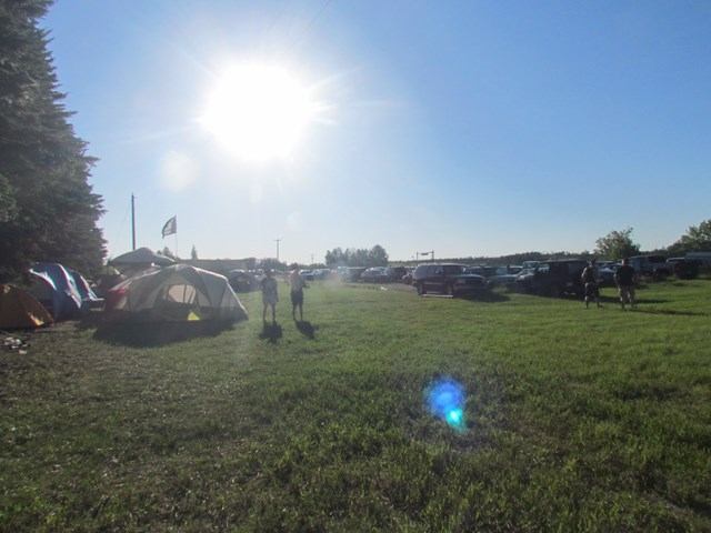 Tents and people on grassy field with sun and trees at Métis Crossing Campground.