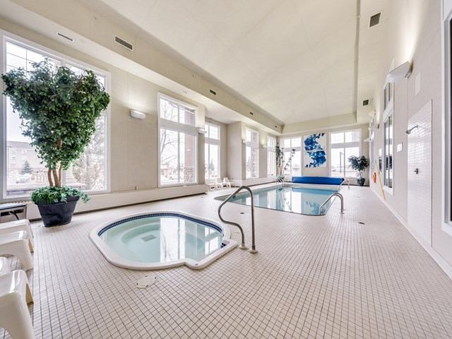 Indoor pool area with hot tub, large windows, and bright tiled flooring.