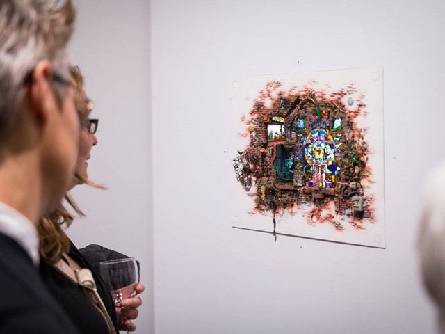 Woman viewing colorful abstract painting on gallery wall with framed artwork nearby.