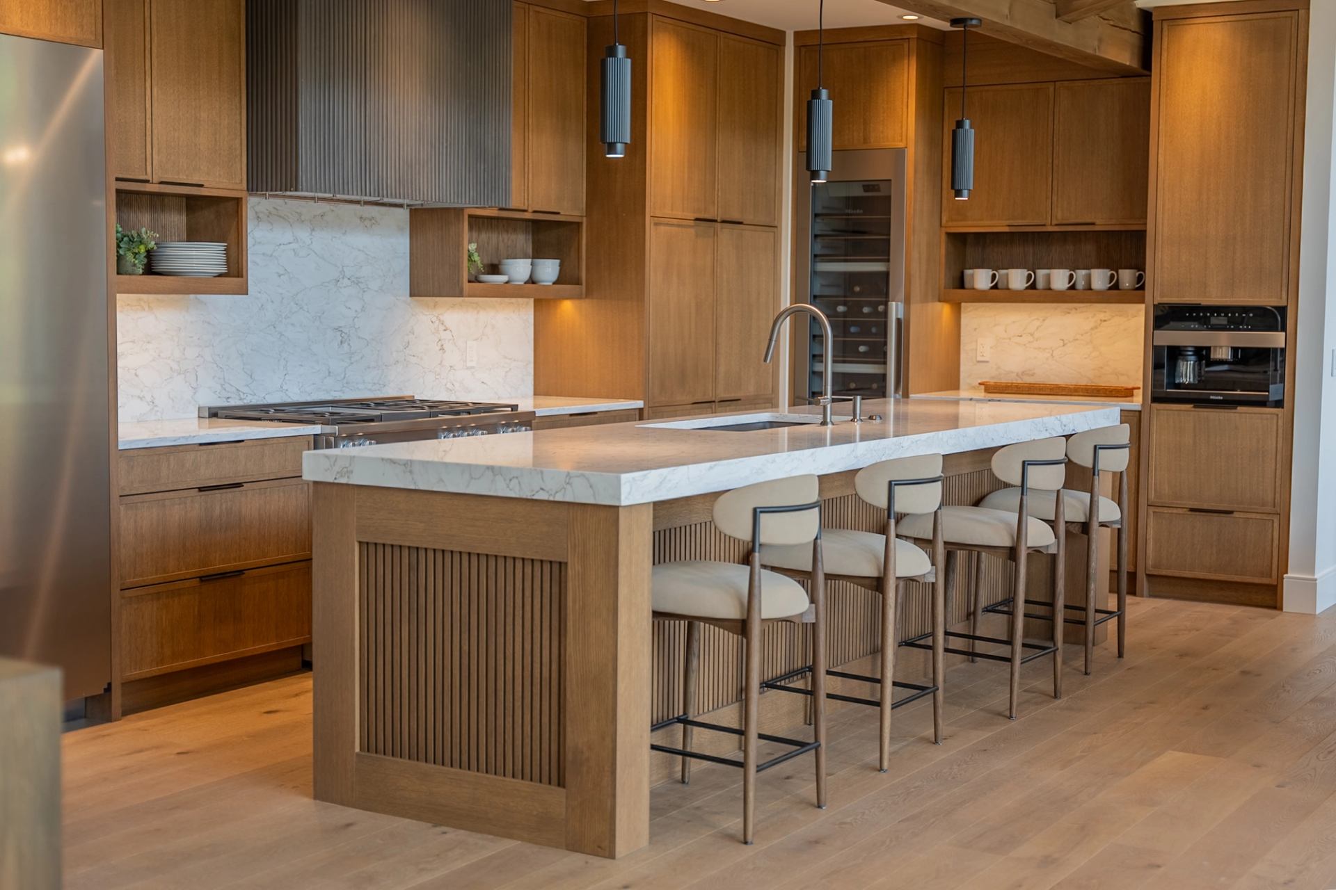 A contemporary kitchen features warm wood cabinetry, a large island with seating, pendant lights, and modern appliances.