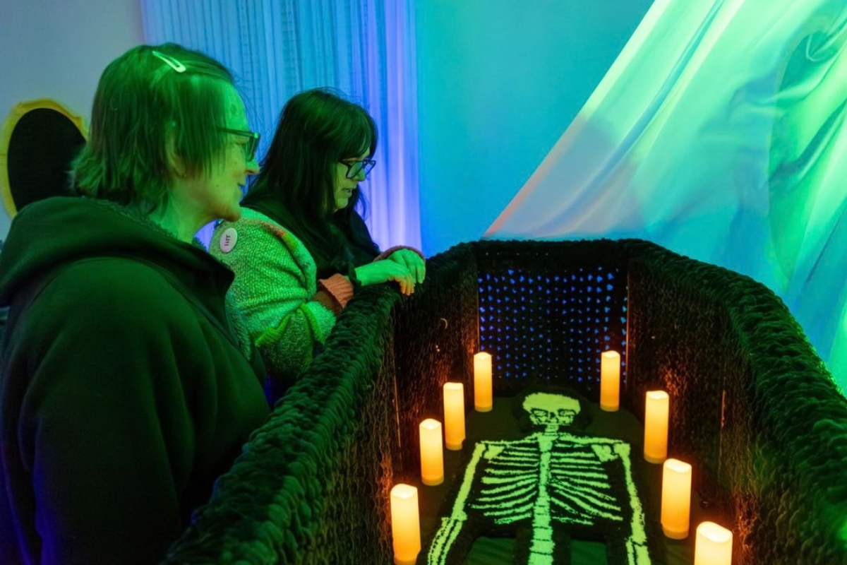 Visitors view a glowing skeleton display surrounded by candles under green and blue lights.