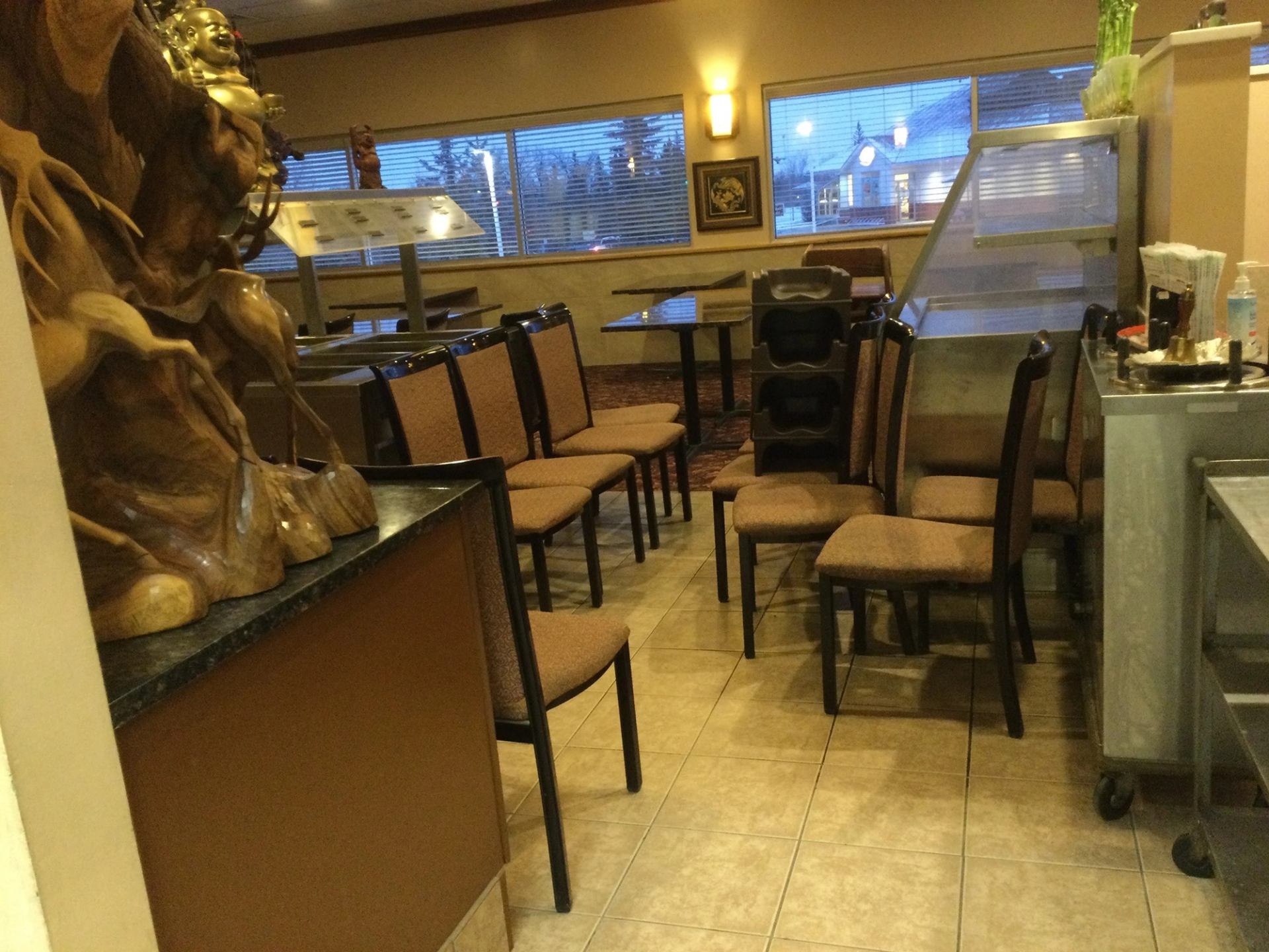 Restaurant interior with chairs, statue, tables, and counter near windows.