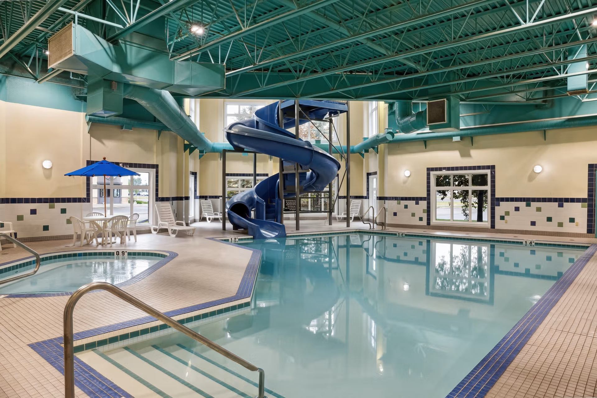 Indoor swimming pool with blue waterslide, hot tub, lounge chairs and umbrella table.