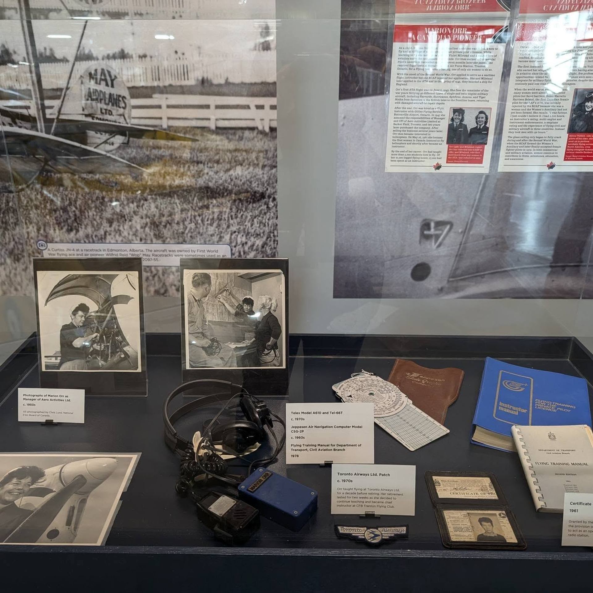 Museum display case with vintage aviation photos, pilot documents, headset and navigation tools.