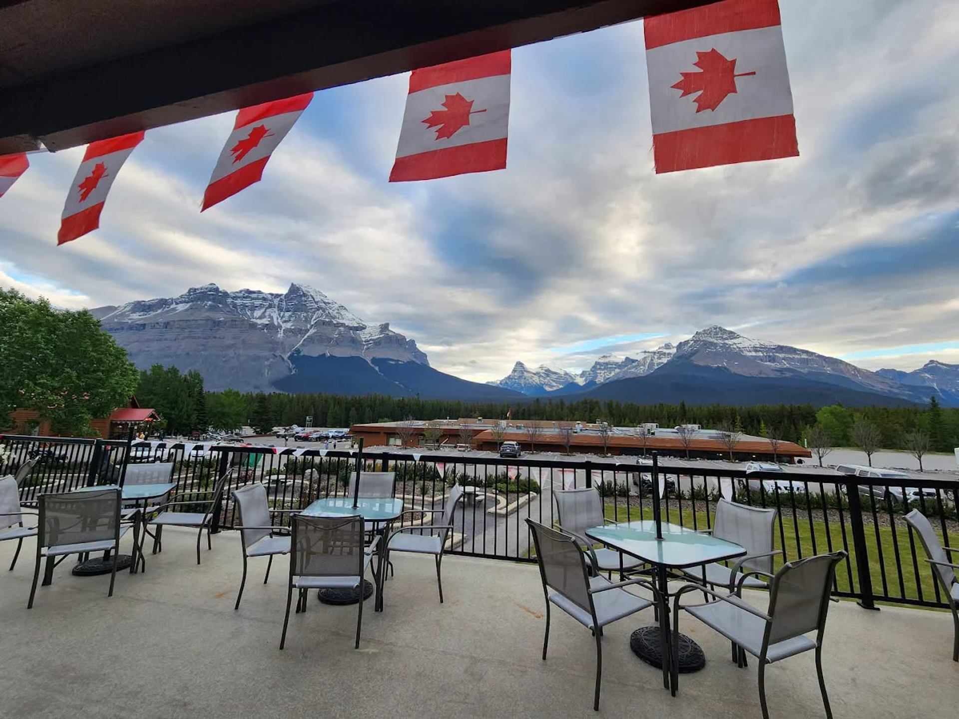 Patio tables under Canadian flags overlooking parking lot and snow-capped mountain range.