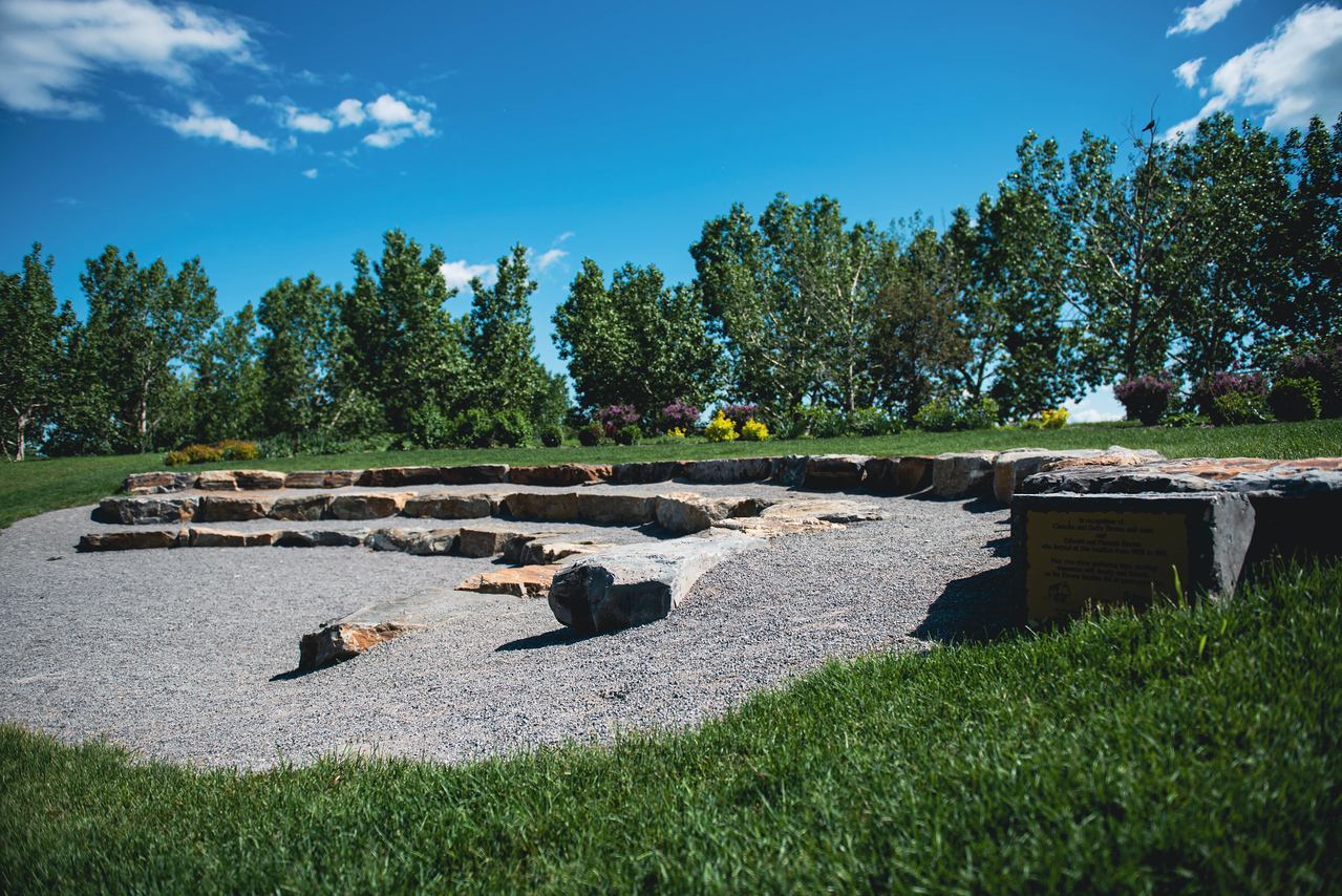 Stone amphitheatre with tiered rock seating in a park, surrounded by trees and grass.