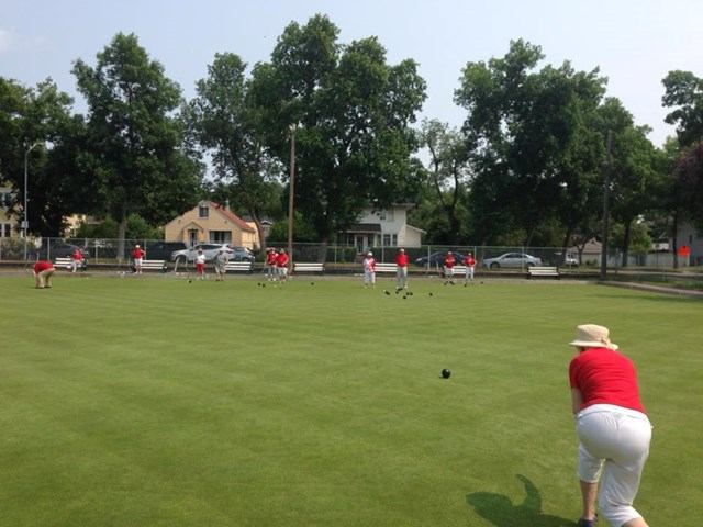 People in red shirts and while pants lawn bowling.