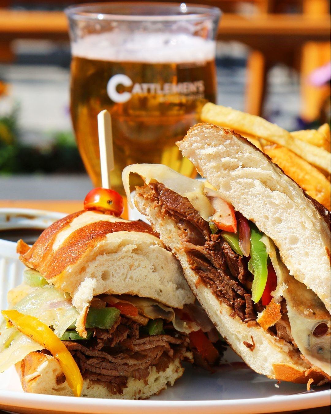 Sandwich with fries and beer featuring Cattleman’s Chophouse logo in the background.