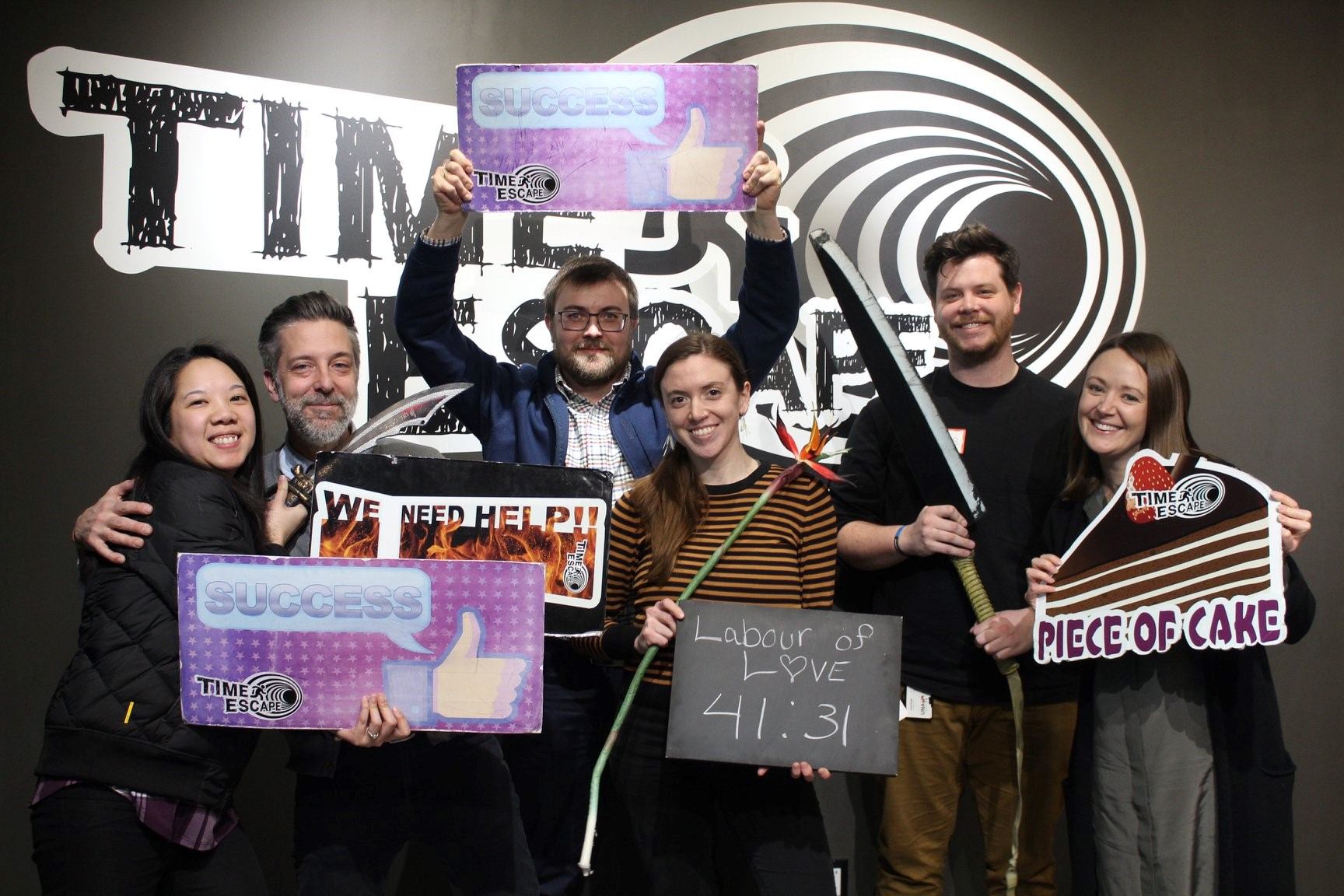 Group posing with Time Escape signs in front of large black-and-white wall mural.