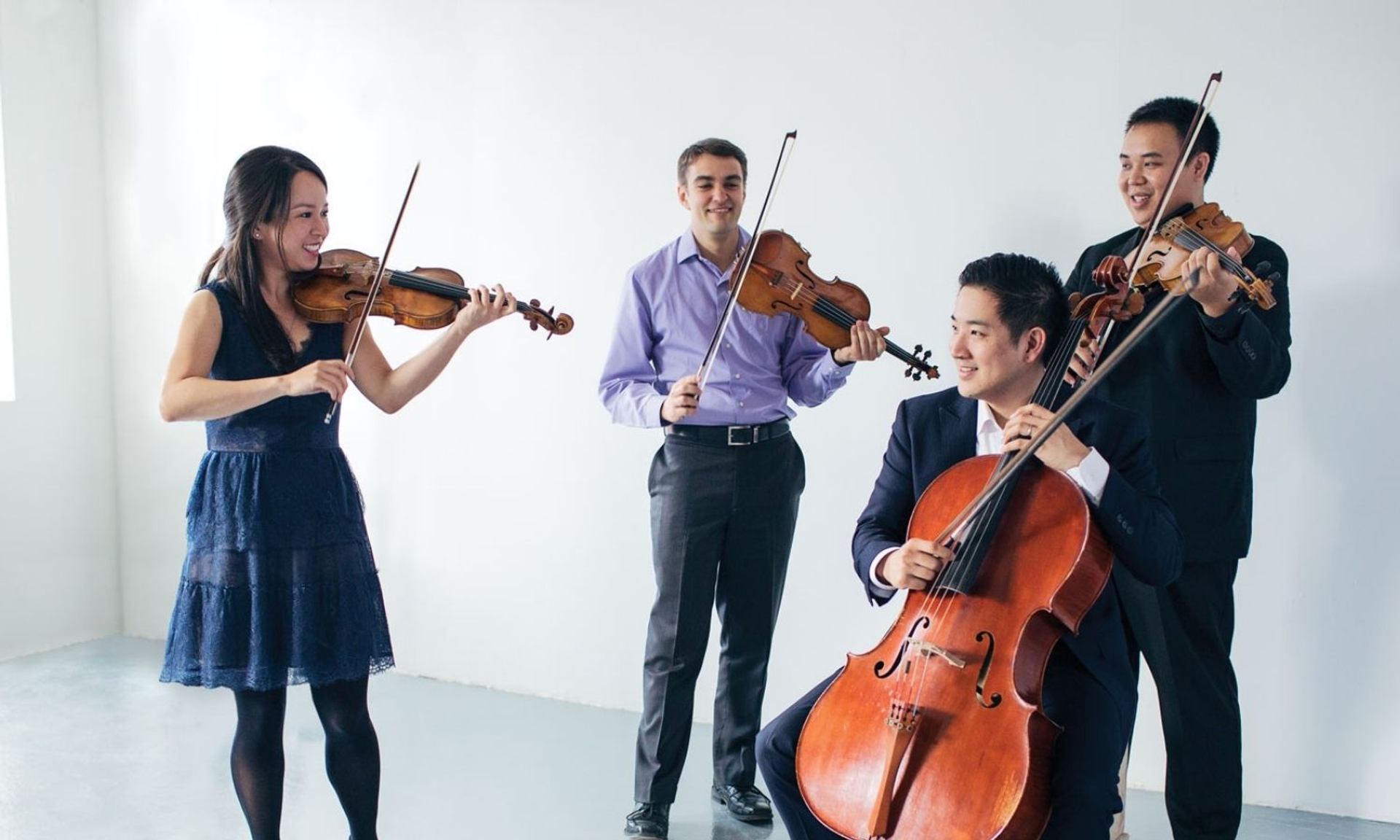 String quartet musicians playing violins and cello together in a bright studio.