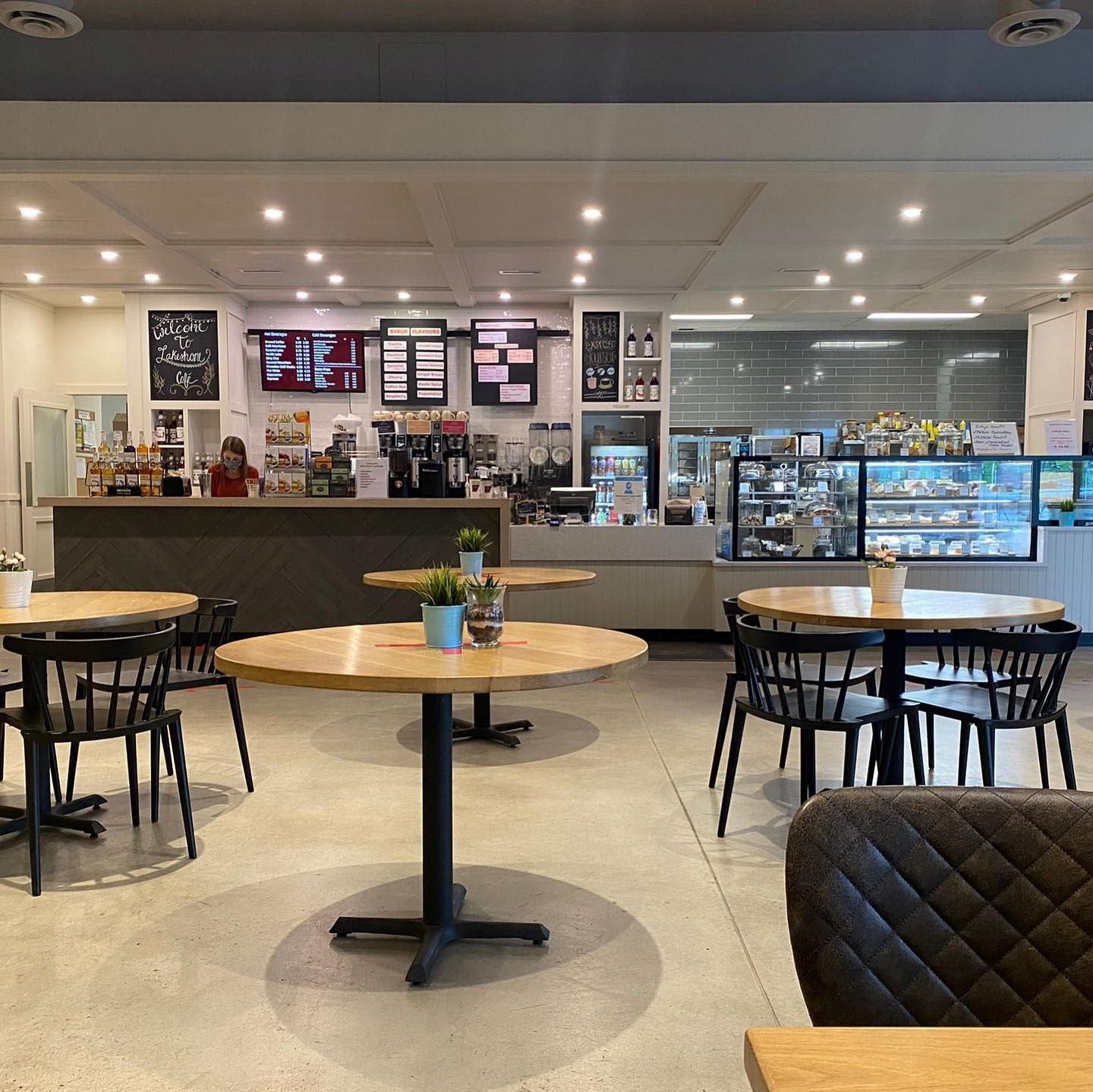 Modern cafe with wood tables, black chairs, and pastry counter.