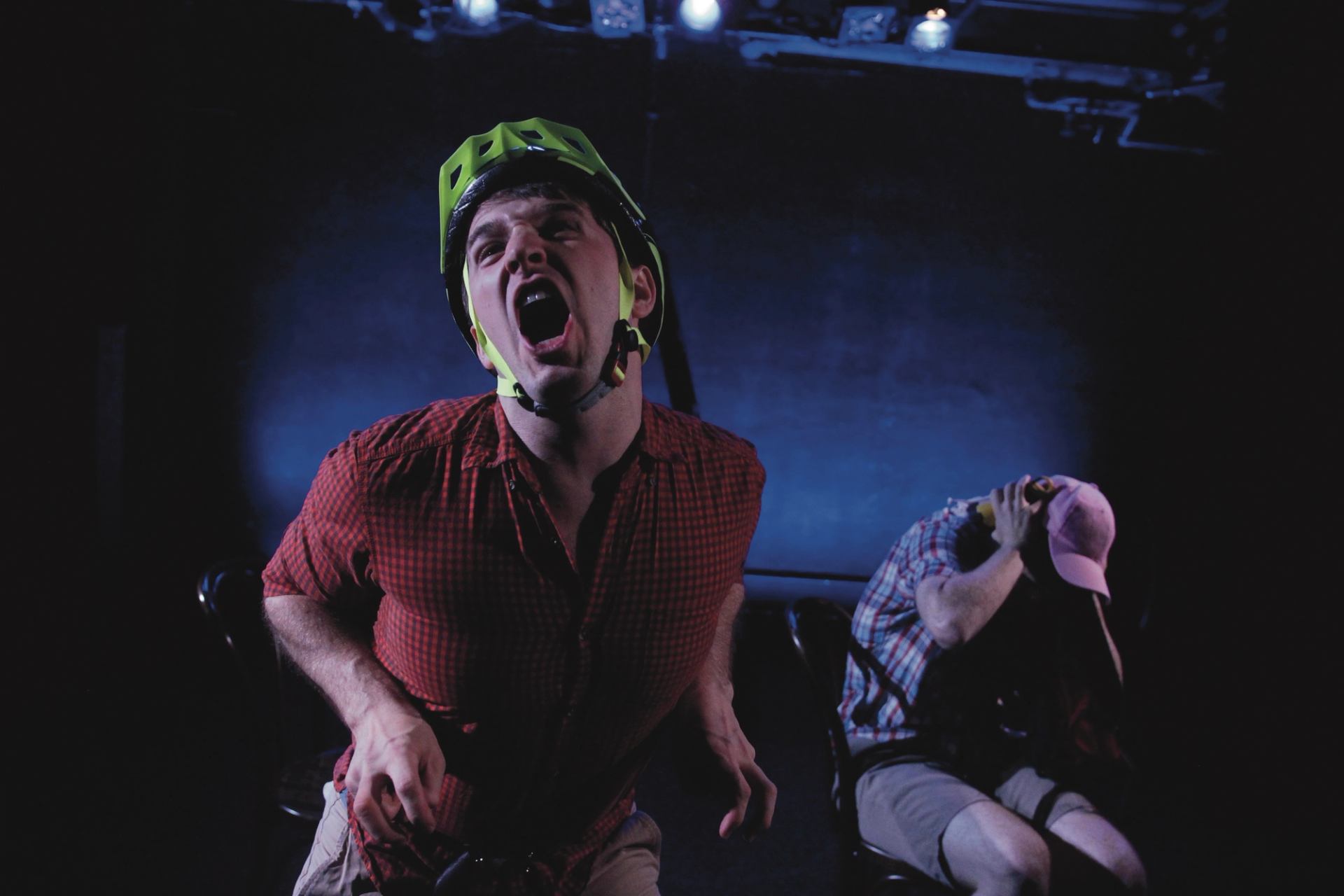 Stage performance with two people in helmets, one shouting, one hunched over.