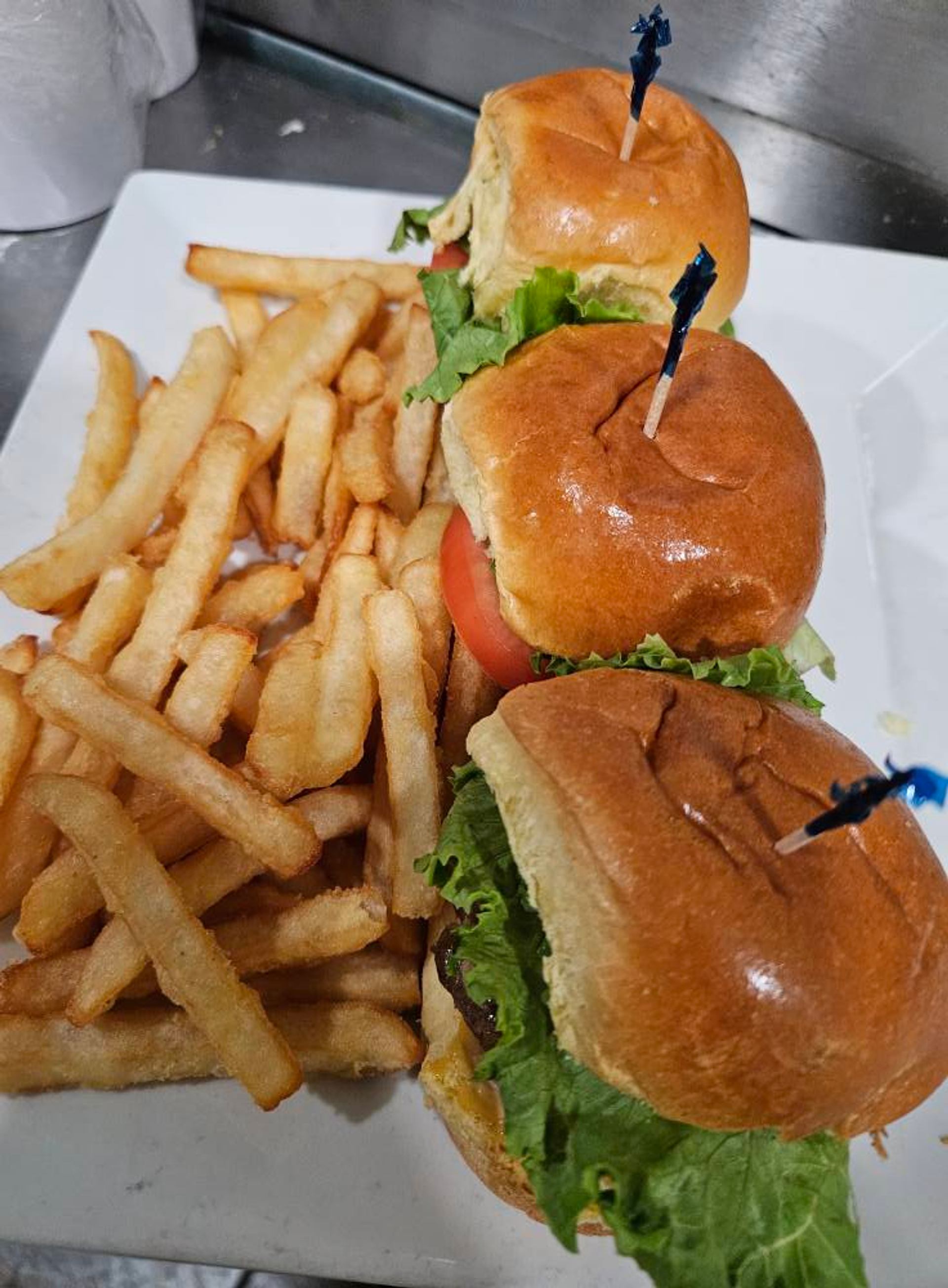 Plate of three slider burgers with lettuce and tomato beside a pile of fries.