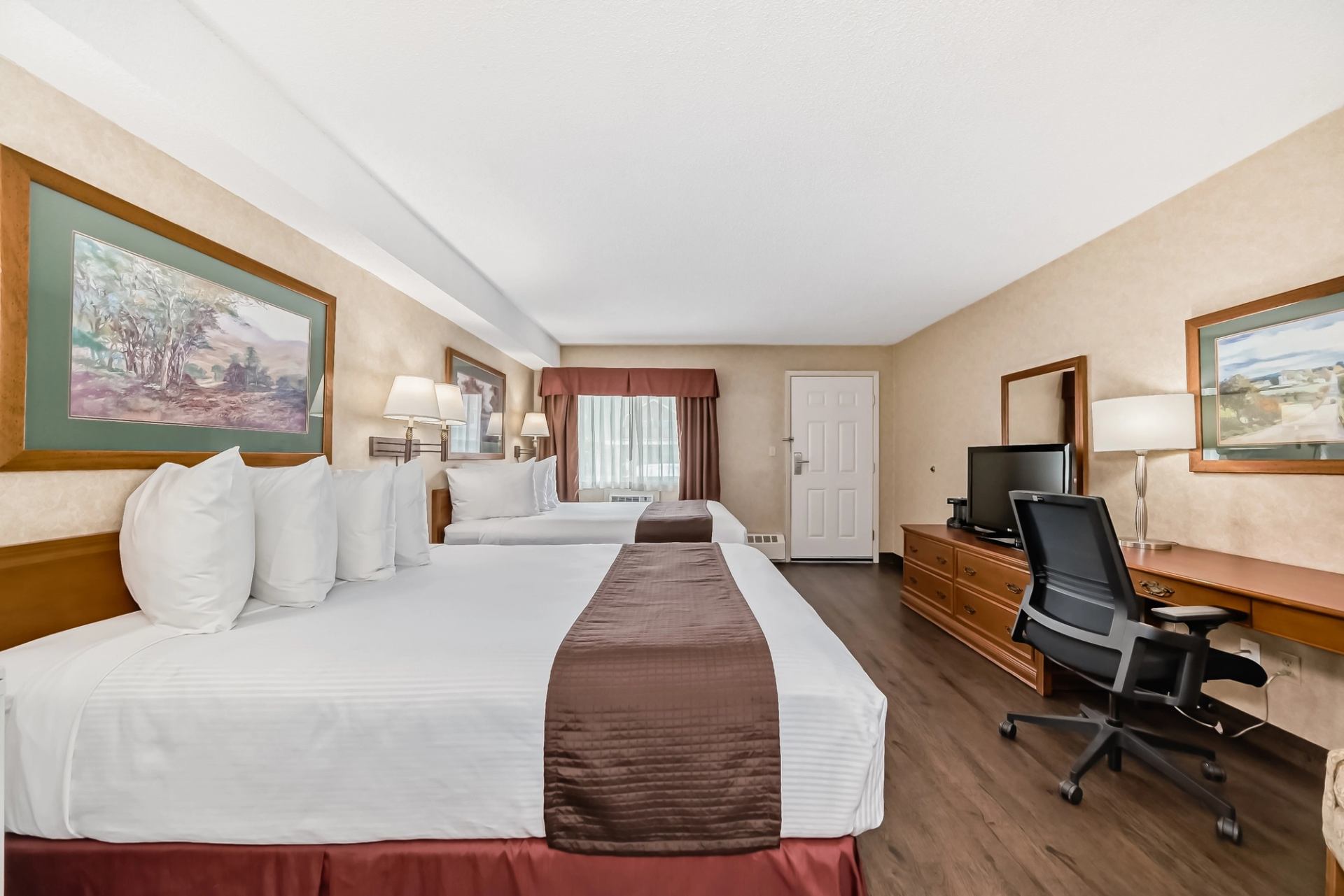 Hotel room featuring two beds, a work desk, flat-screen TV, and framed artwork