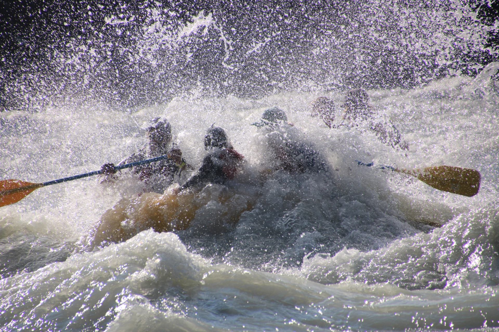 Raft nearly hidden by a crashing wave as it pushes through heavy whitewater.