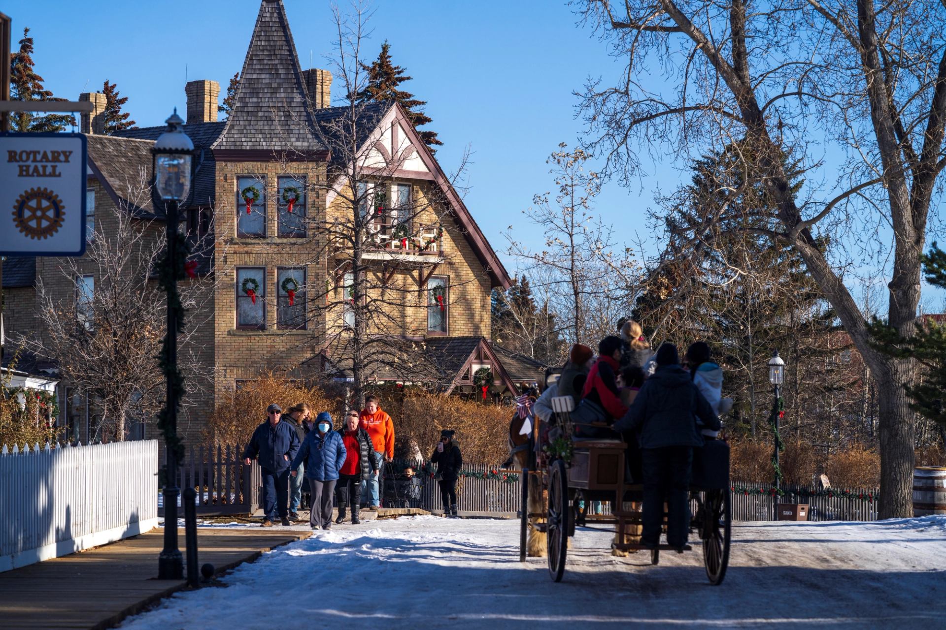 Horse-drawn wagon carries visitors along a snowy path past historic buildings.