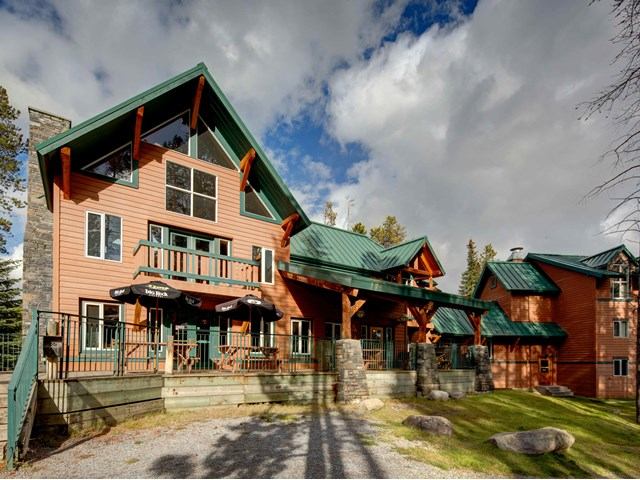 Lodge-style building with green roof and balconies in a forested mountain setting.
