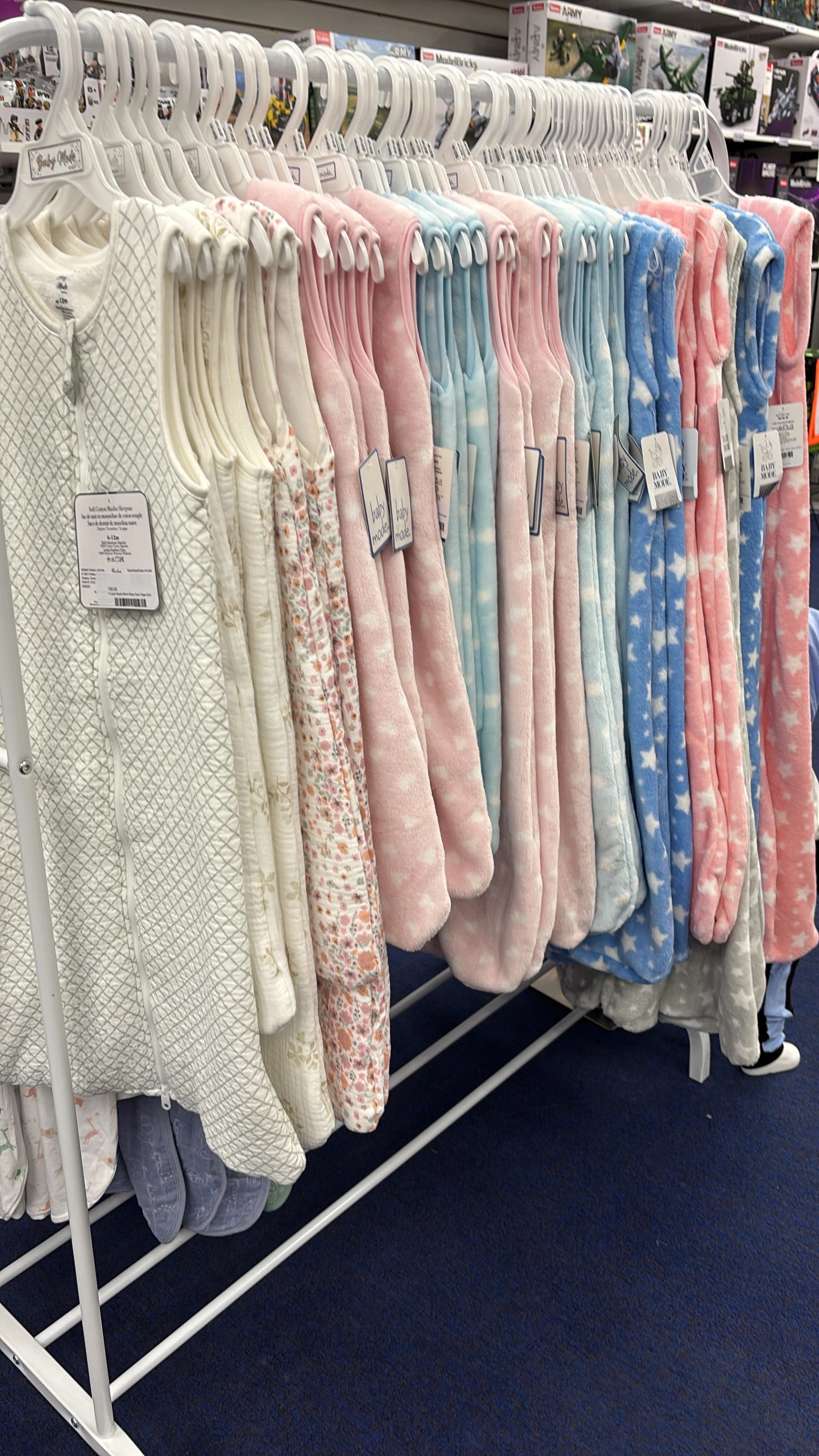 Rack of pastel children’s sleep sacks and quilted garments neatly hung on white hangers in a shop.
