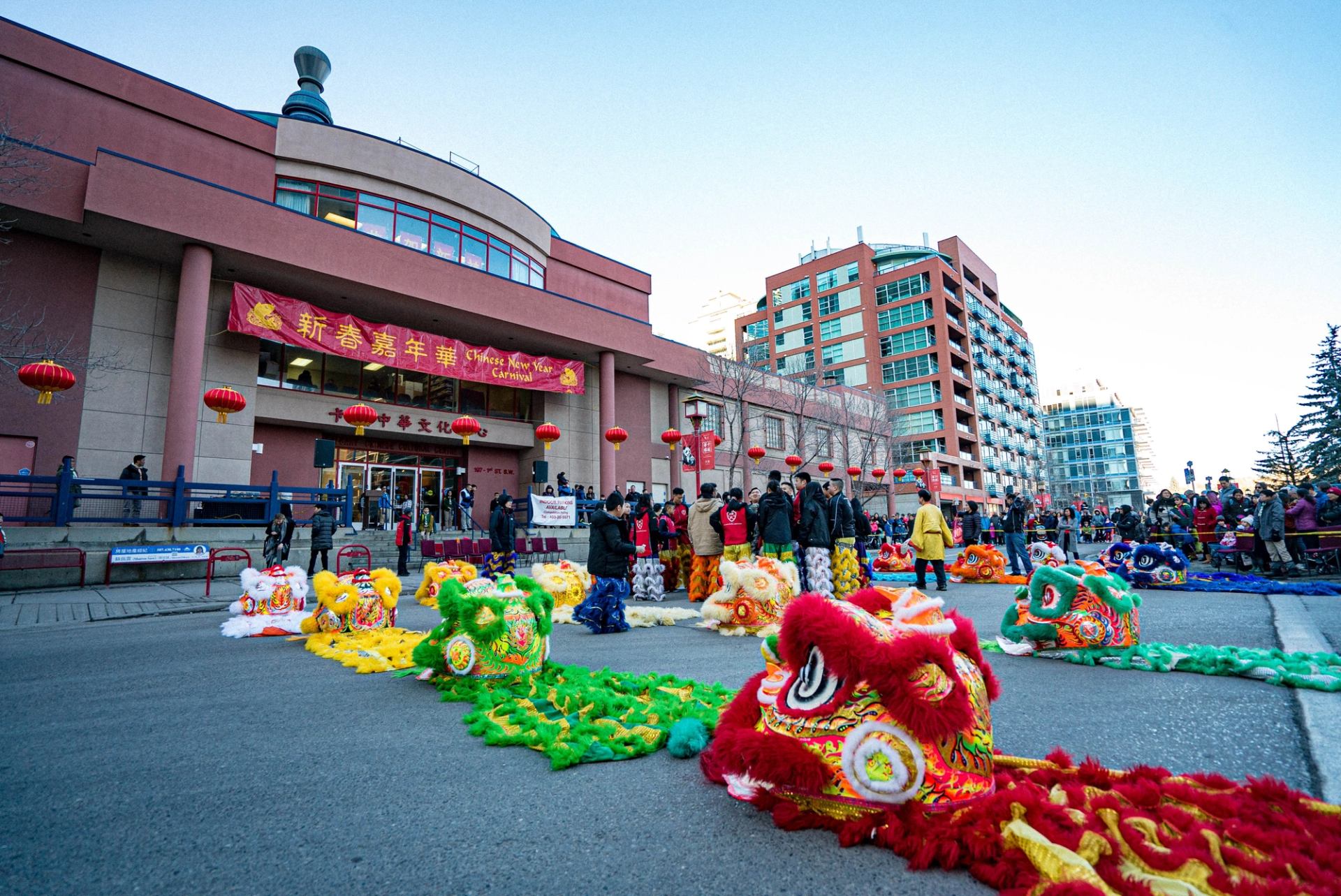 Chinese New Year celebration with colorful lion heads and lanterns outside a city building.