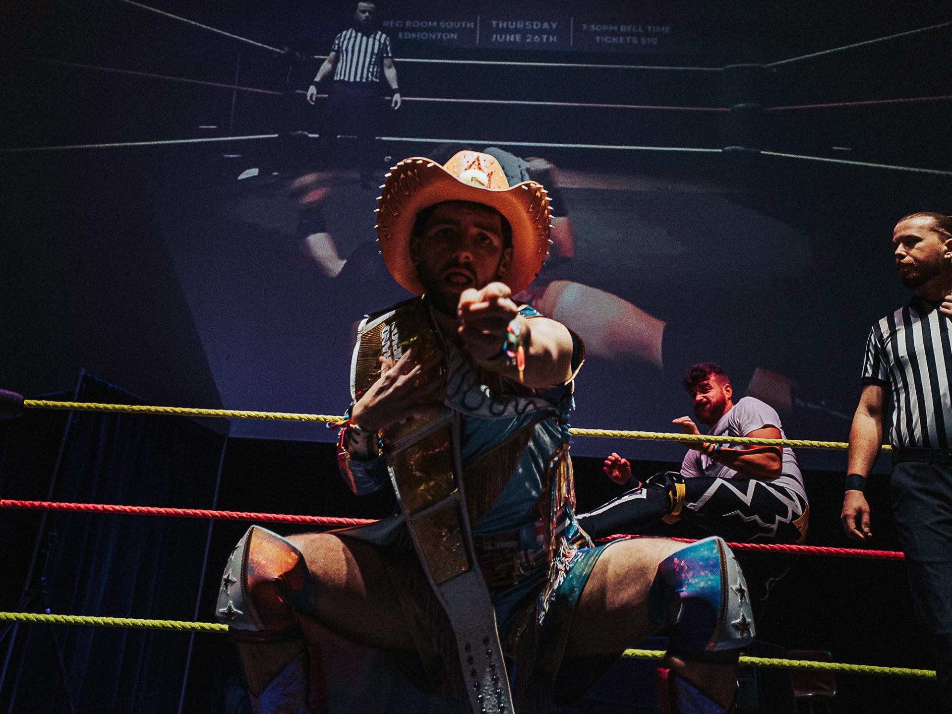 Wrestler in cowboy hat points at camera during Love Pro Wrestling match.