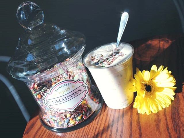 Jar of Smarties next to a creamy milkshake topped with sprinkles and a yellow flower