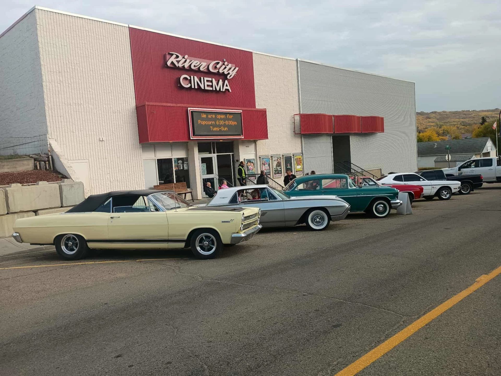 Classic cars parked outside River City Cinema with red awnings and marquee sign.