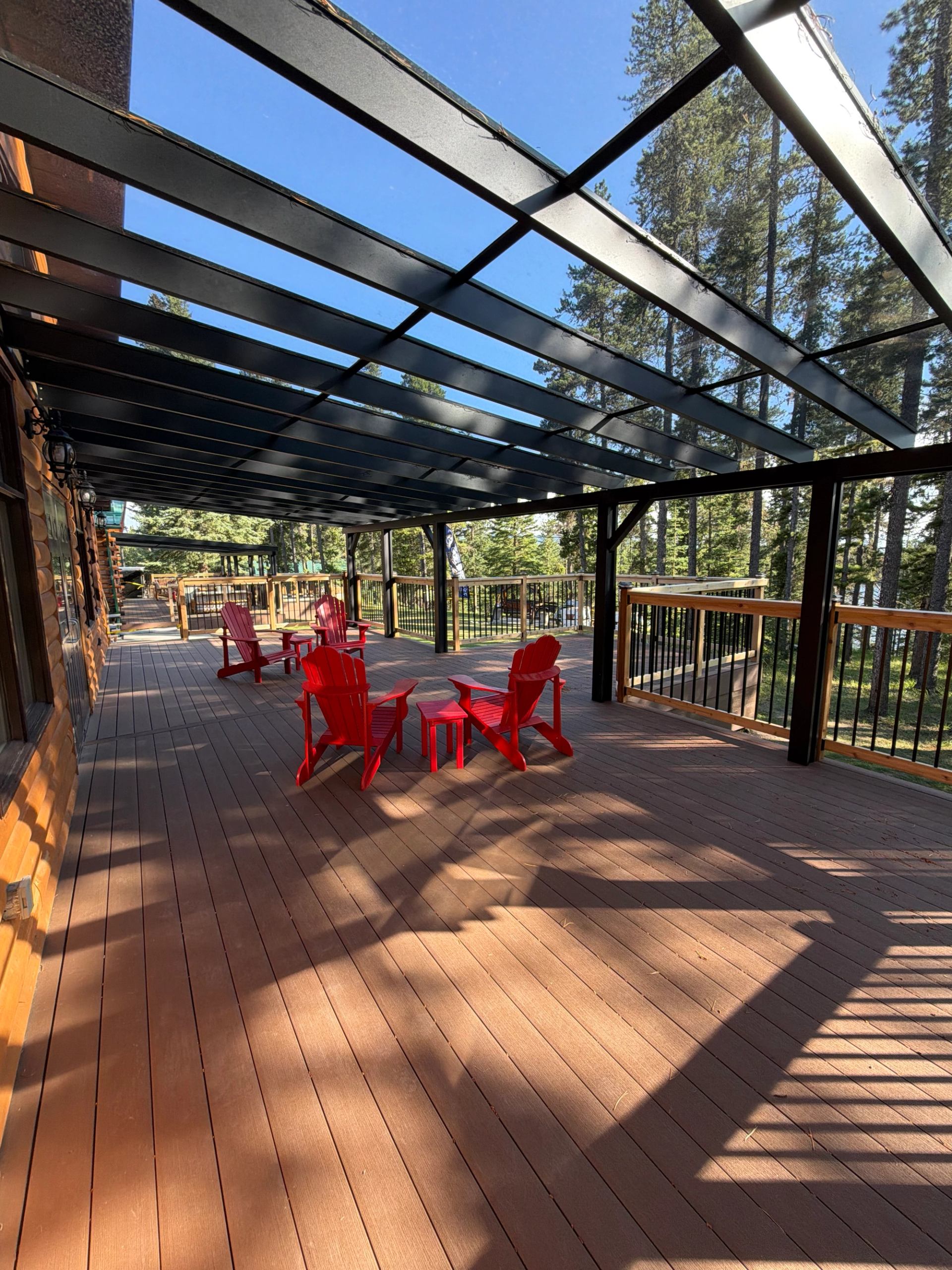 Covered wooden deck with red Adirondack chairs overlooking tall evergreen trees.