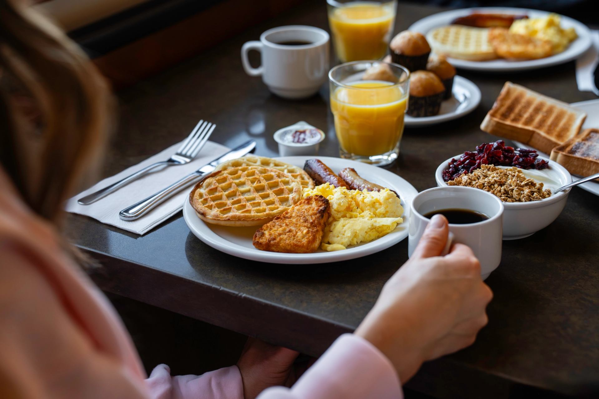 Brekafast foods including waffles, eggs, yogurt bowls with coffee and orange juice