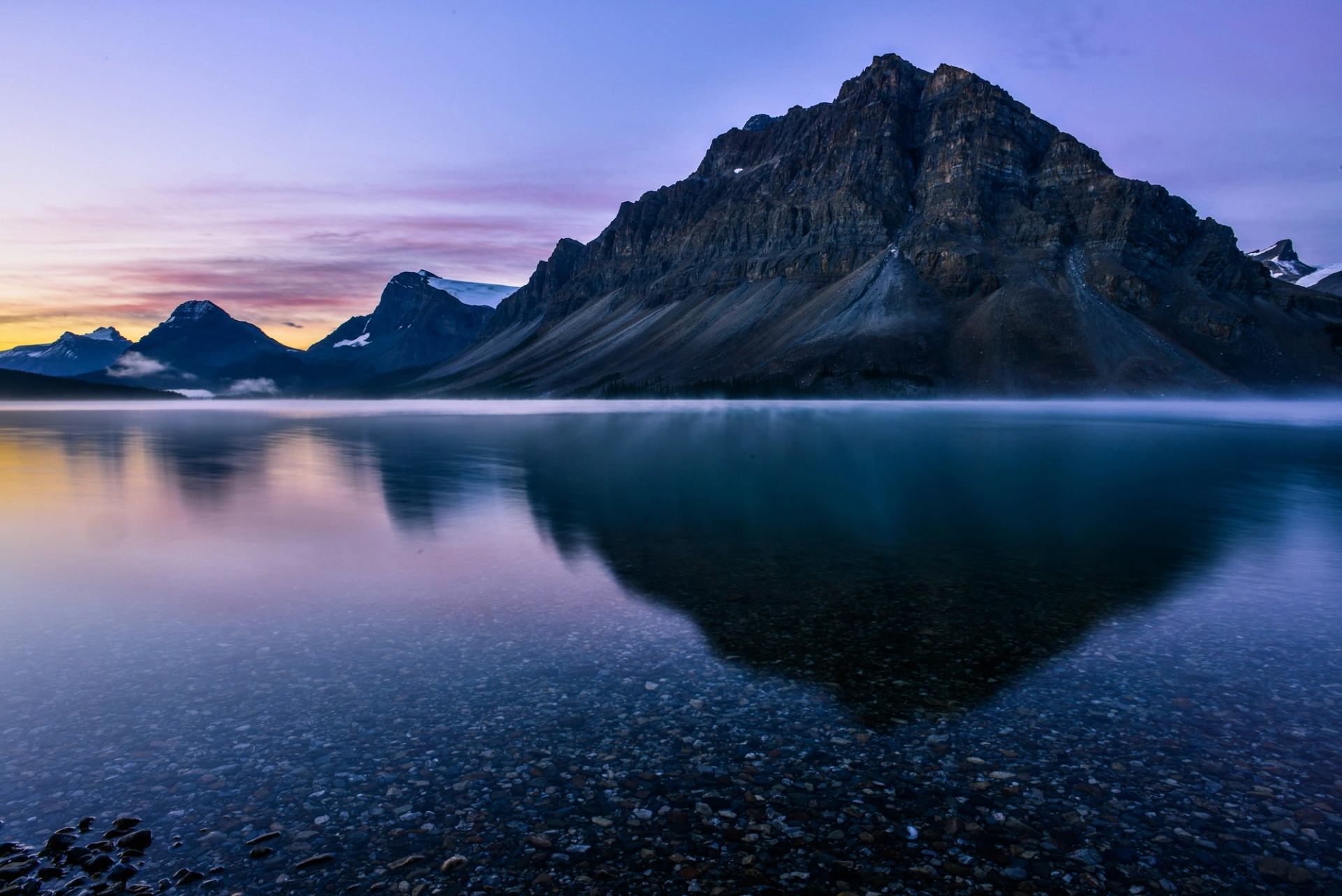 Rocky mountain range reflected in calm lake with clear water and colourful sky.