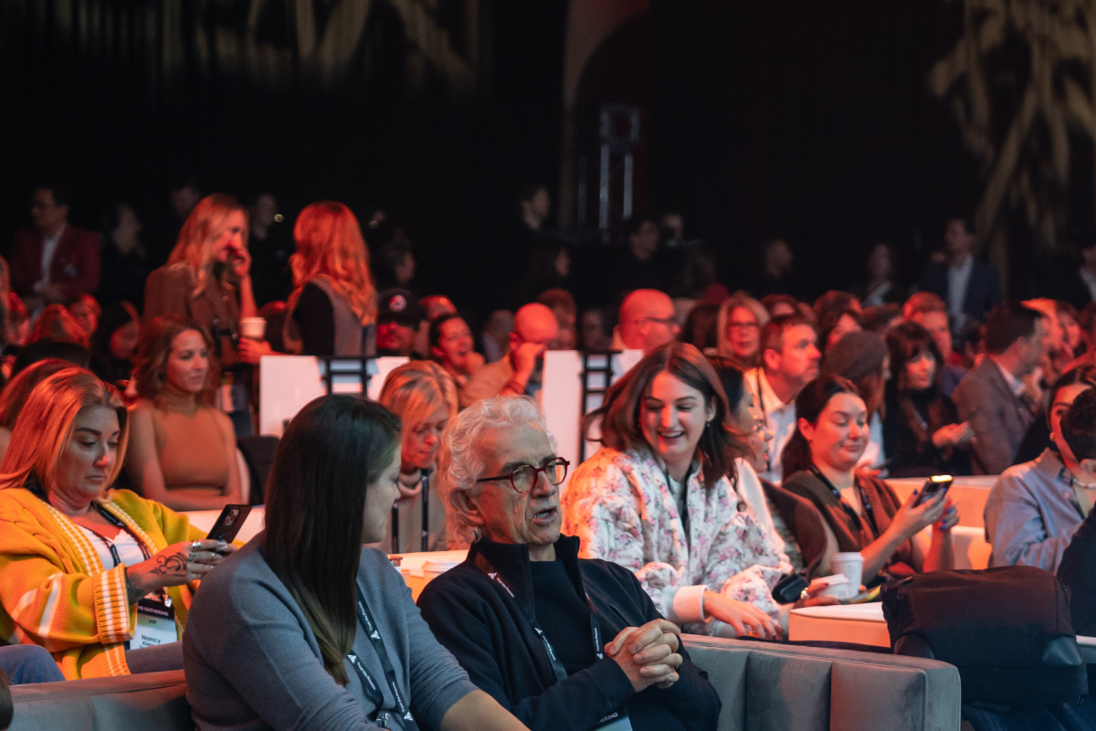 Audience seated in an auditorium during a live event, many people holding phones or papers.