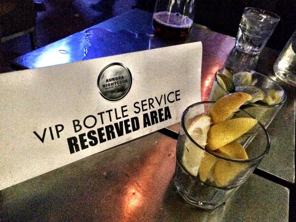 VIP bottle service reserved sign and cocktail glass with citrus slices on a bar table.