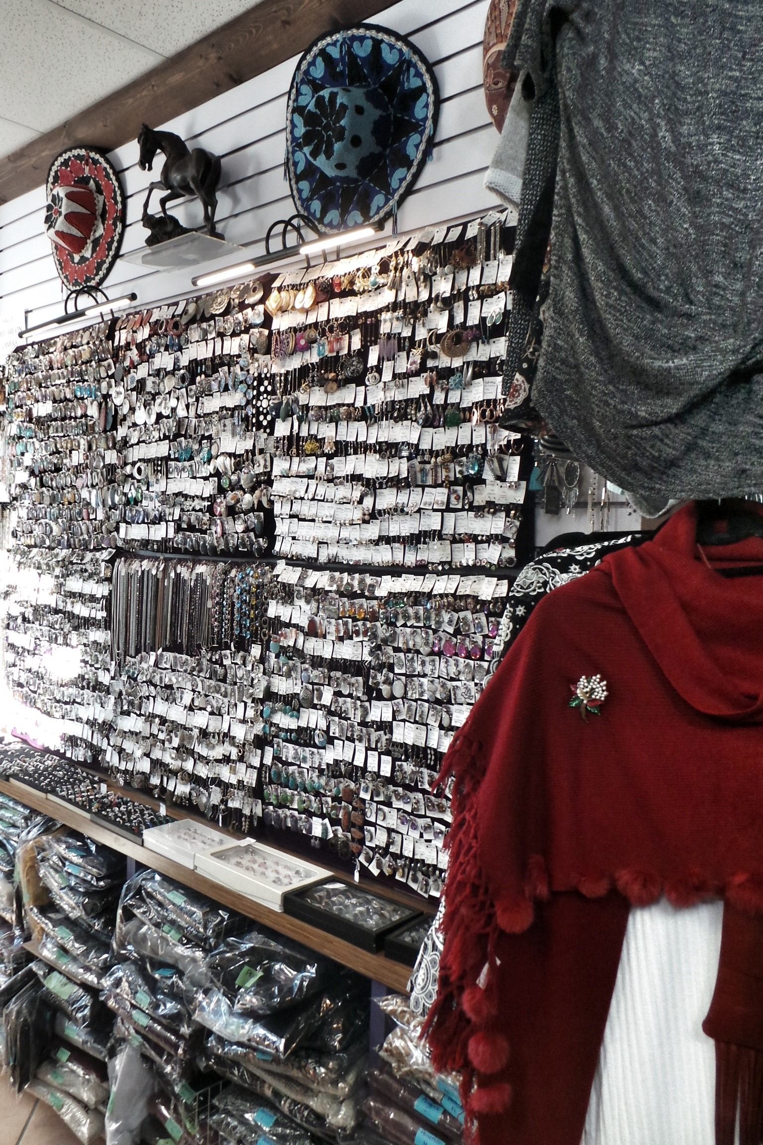 Jewellery wall display with hanging earrings, scarves and mannequin in red shawl.