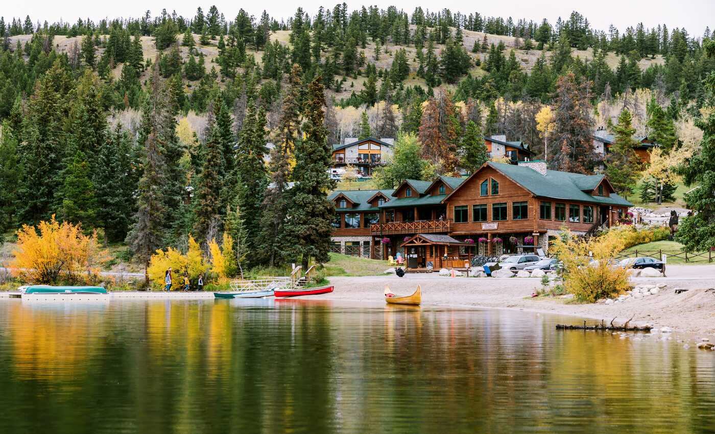 Brightly colored canoes rest a the lakeside with the Pyramid Lake Lodge and treed mountains in the background.