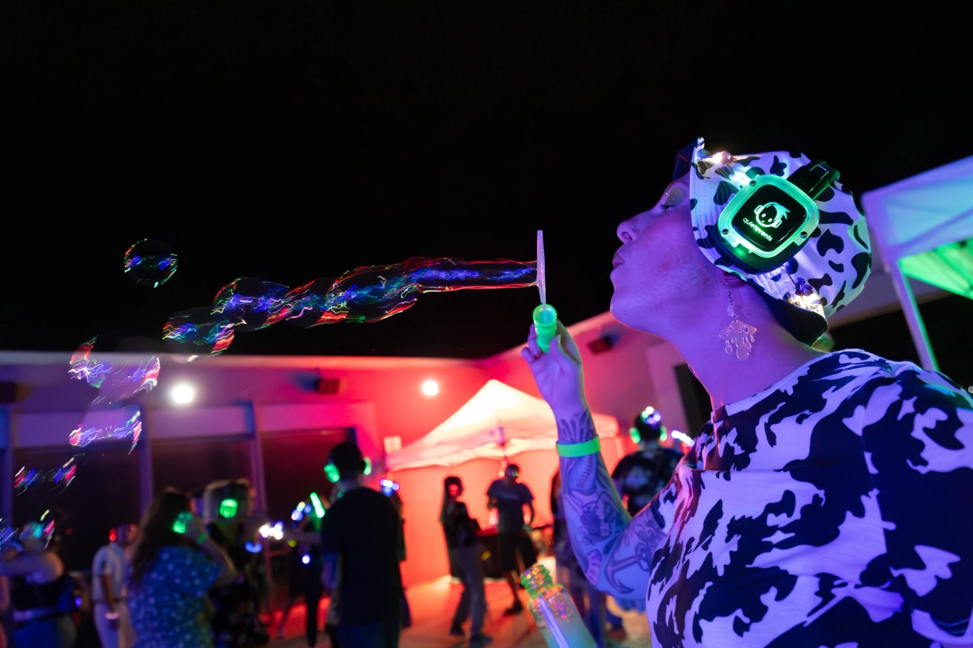 Person blowing soap bubbles at neon silent disco party with glowing headphones.