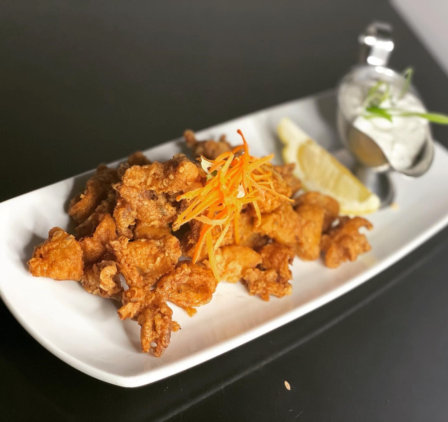 Crispy fried bites tossed in sauce, garnished with shredded carrots on a white plate.