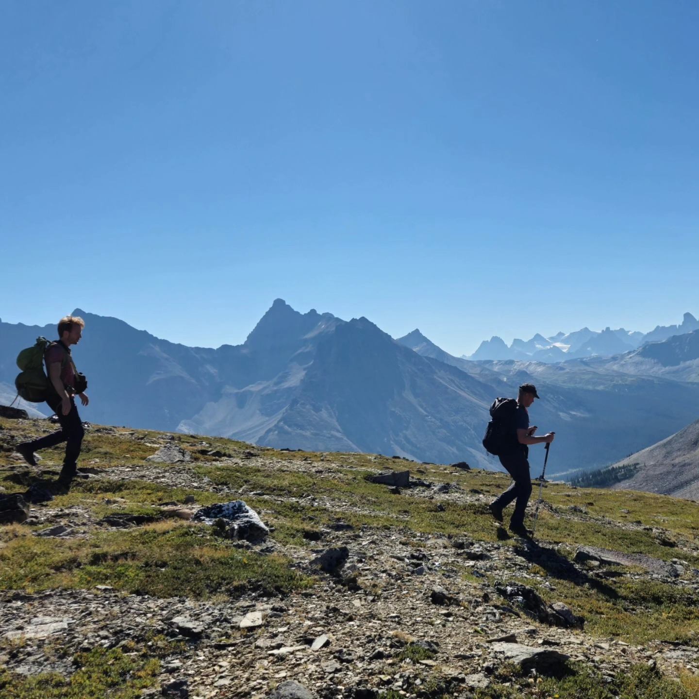 Hikers on rocky trail with backpacks, overlooking mountain peaks in Jasper.