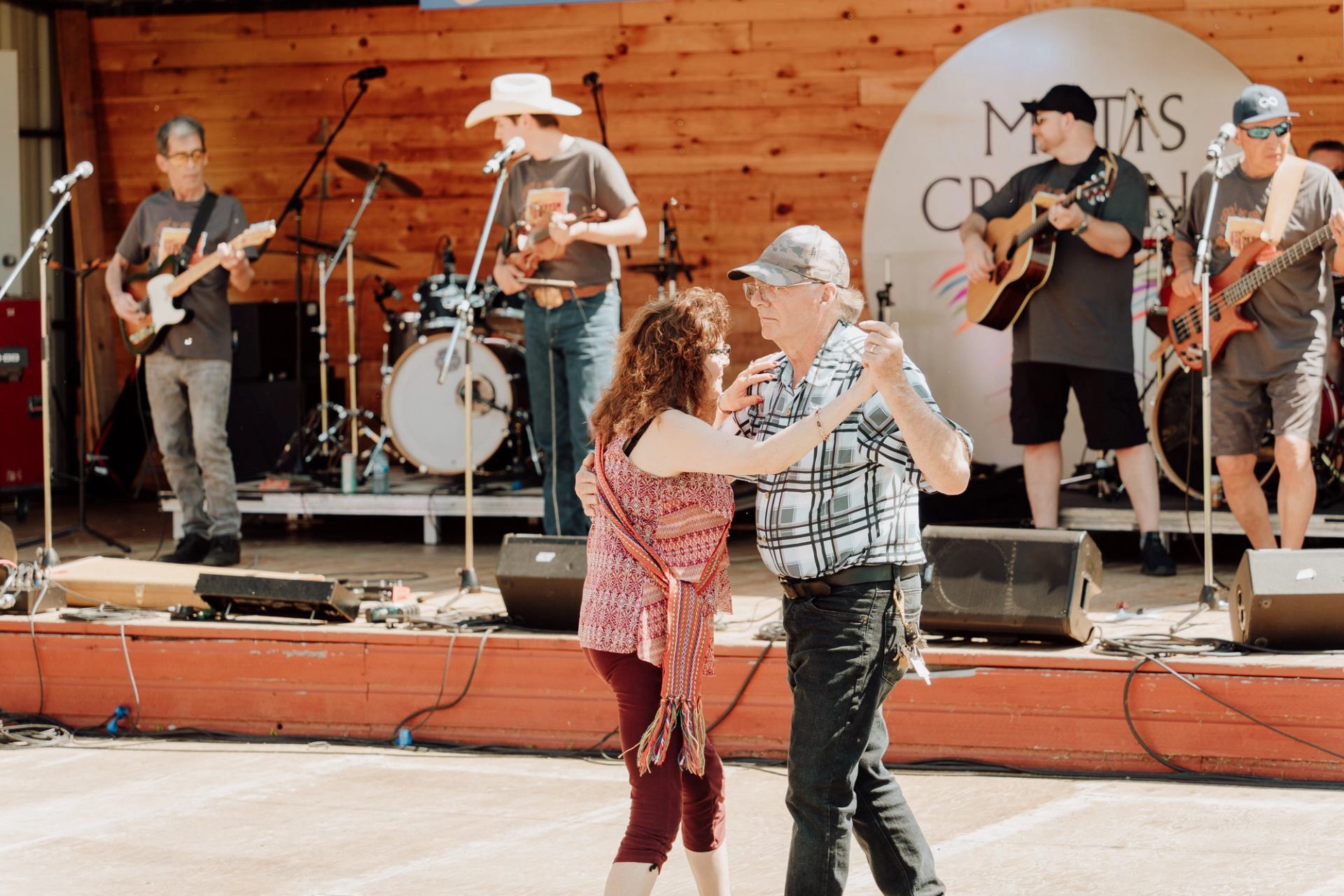 Couple dances in front of live band performing on outdoor wooden stage.