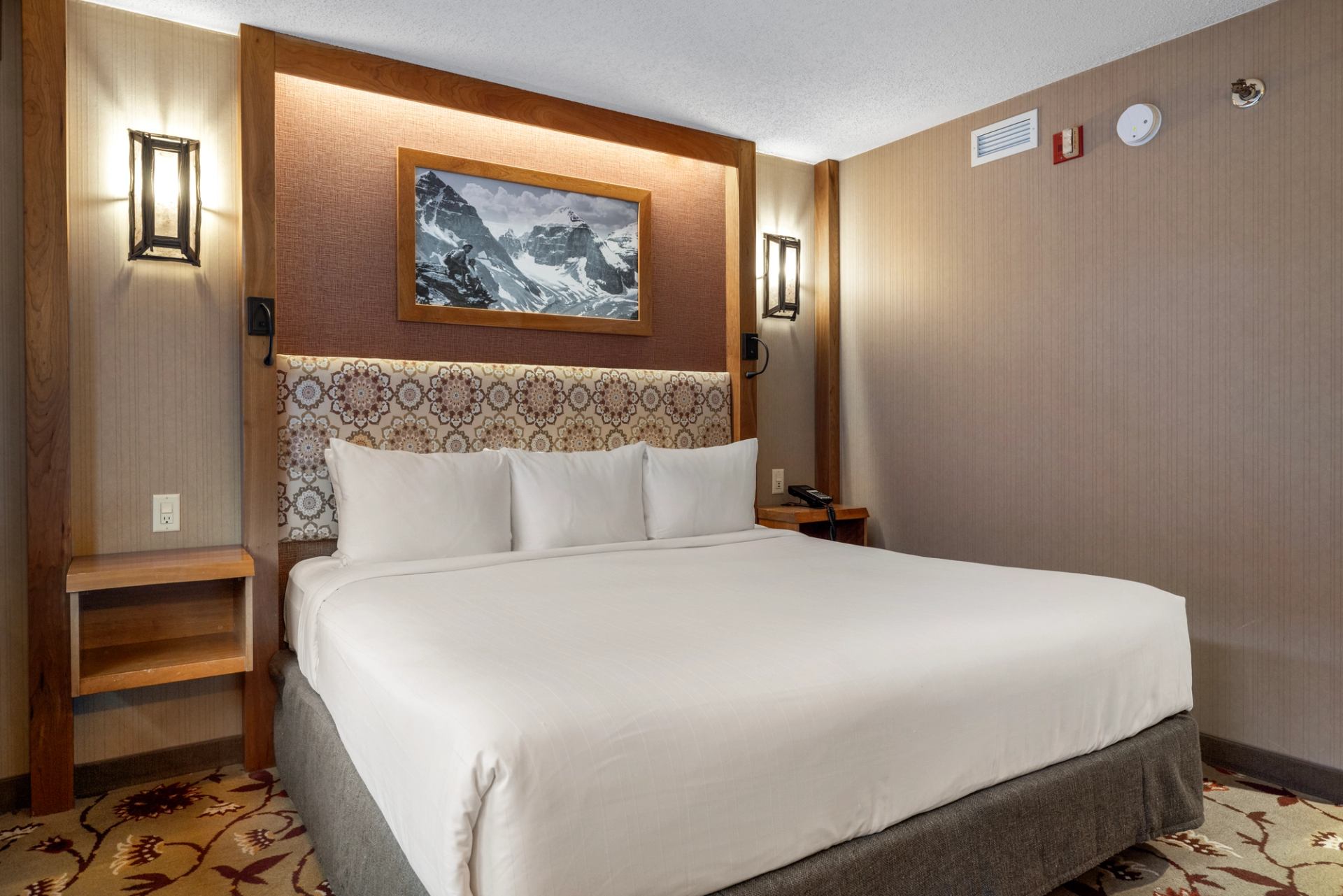 Cozy hotel room with mountain art, white linens, and warm lighting.