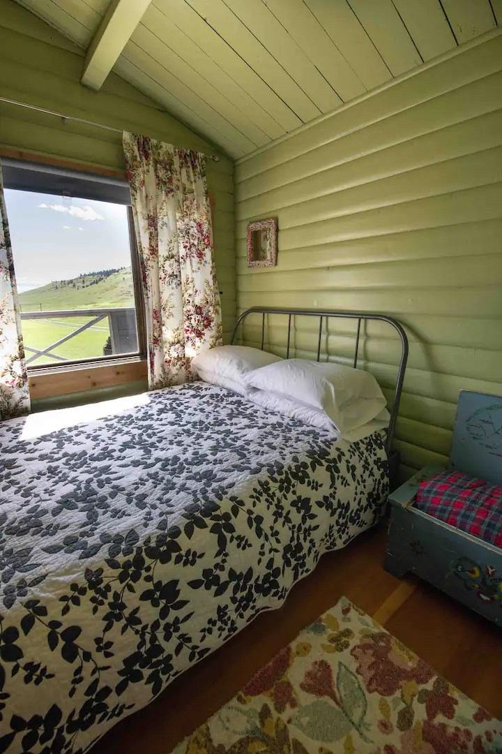 Small bedroom with green paneled walls, floral curtains, and patterned bedspread near a window.