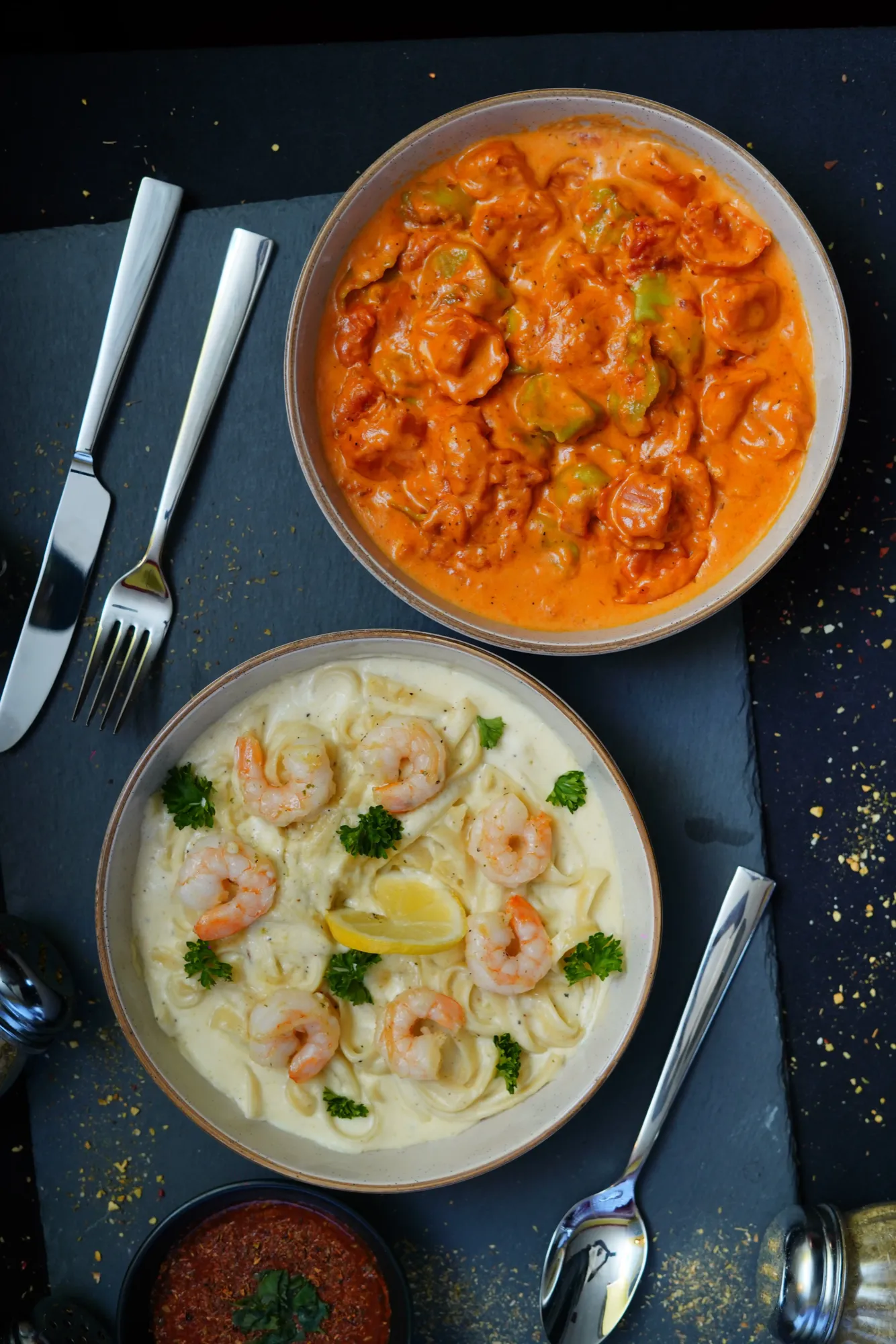Bowls of shrimp pasta in white and tomato sauces with cutlery.