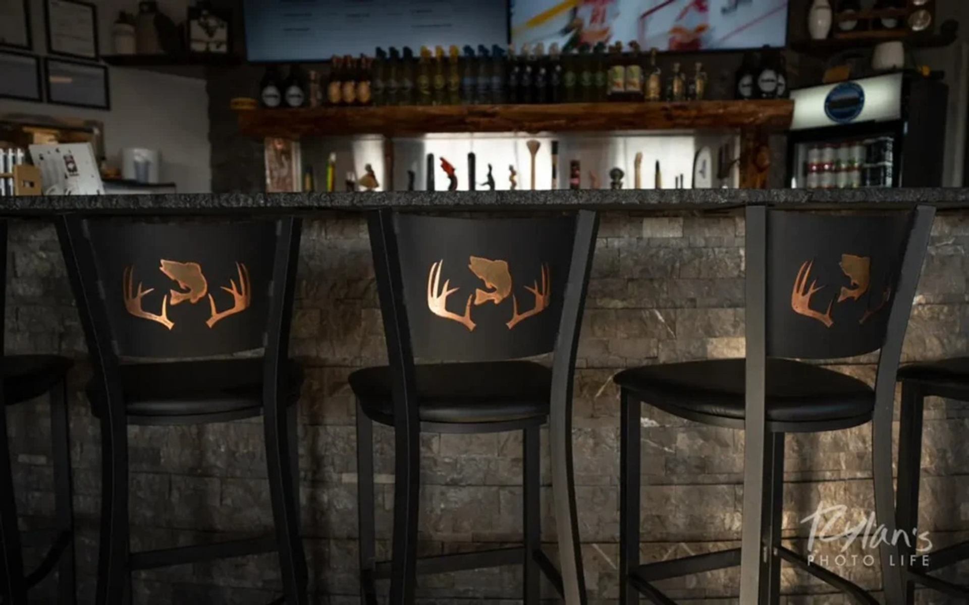 Bar stools with deer antler designs in front of stone bar and bottle display.
