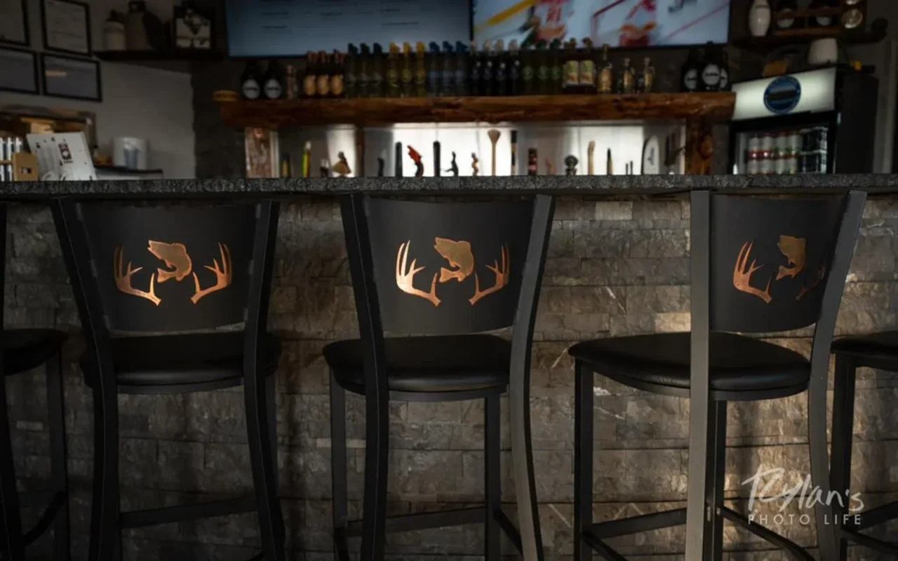 Bar stools with deer antler designs in front of stone bar and bottle display.